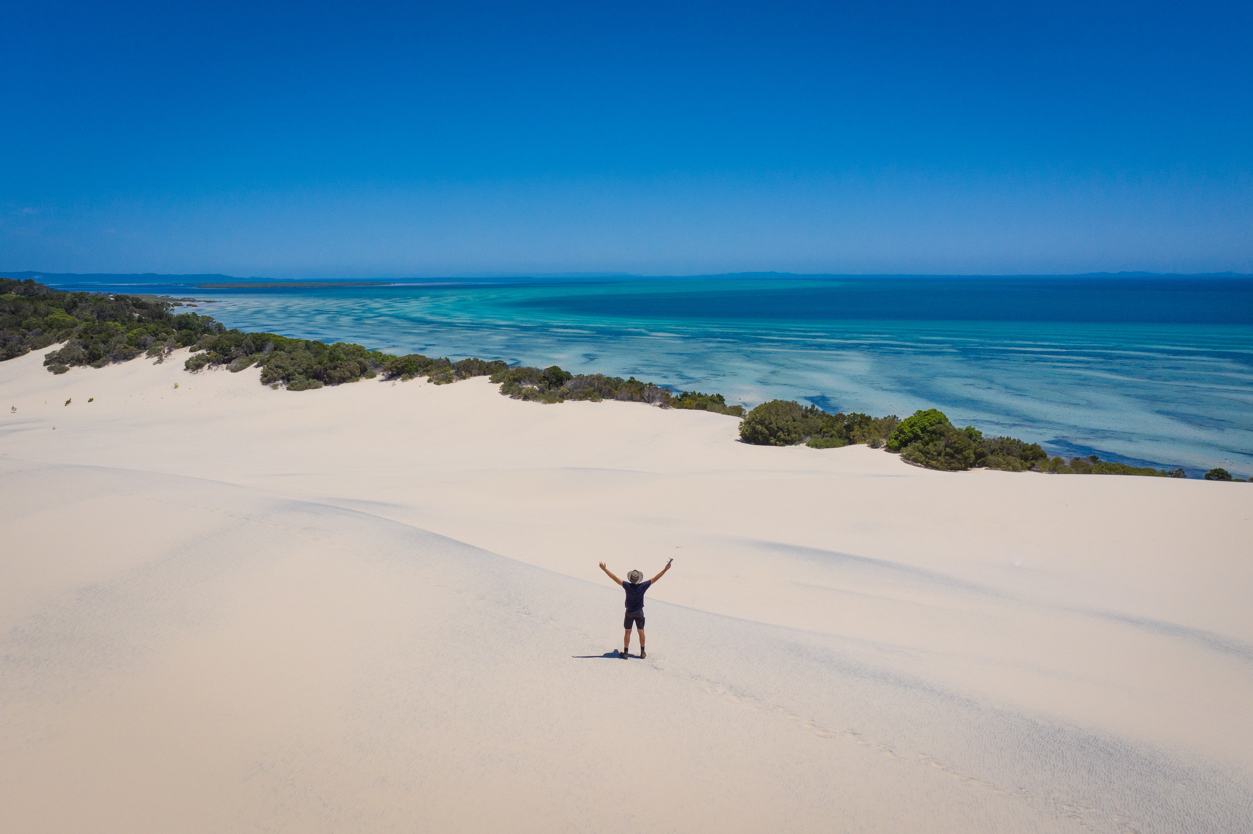 Man stands in middle of huge island sand dunes overlooking ocean