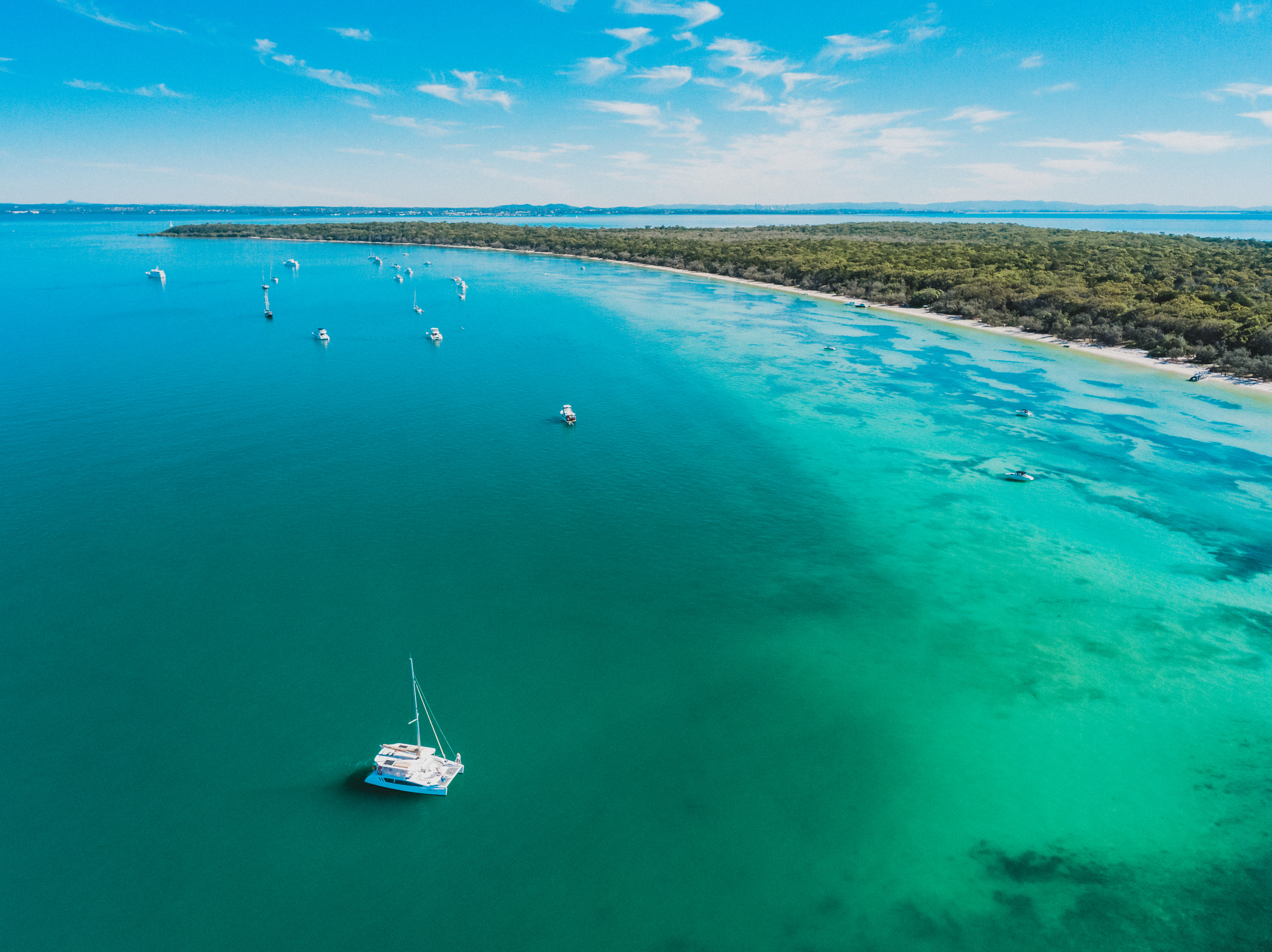 Aerial view of island surrounded by bright blue waters and sailboats 