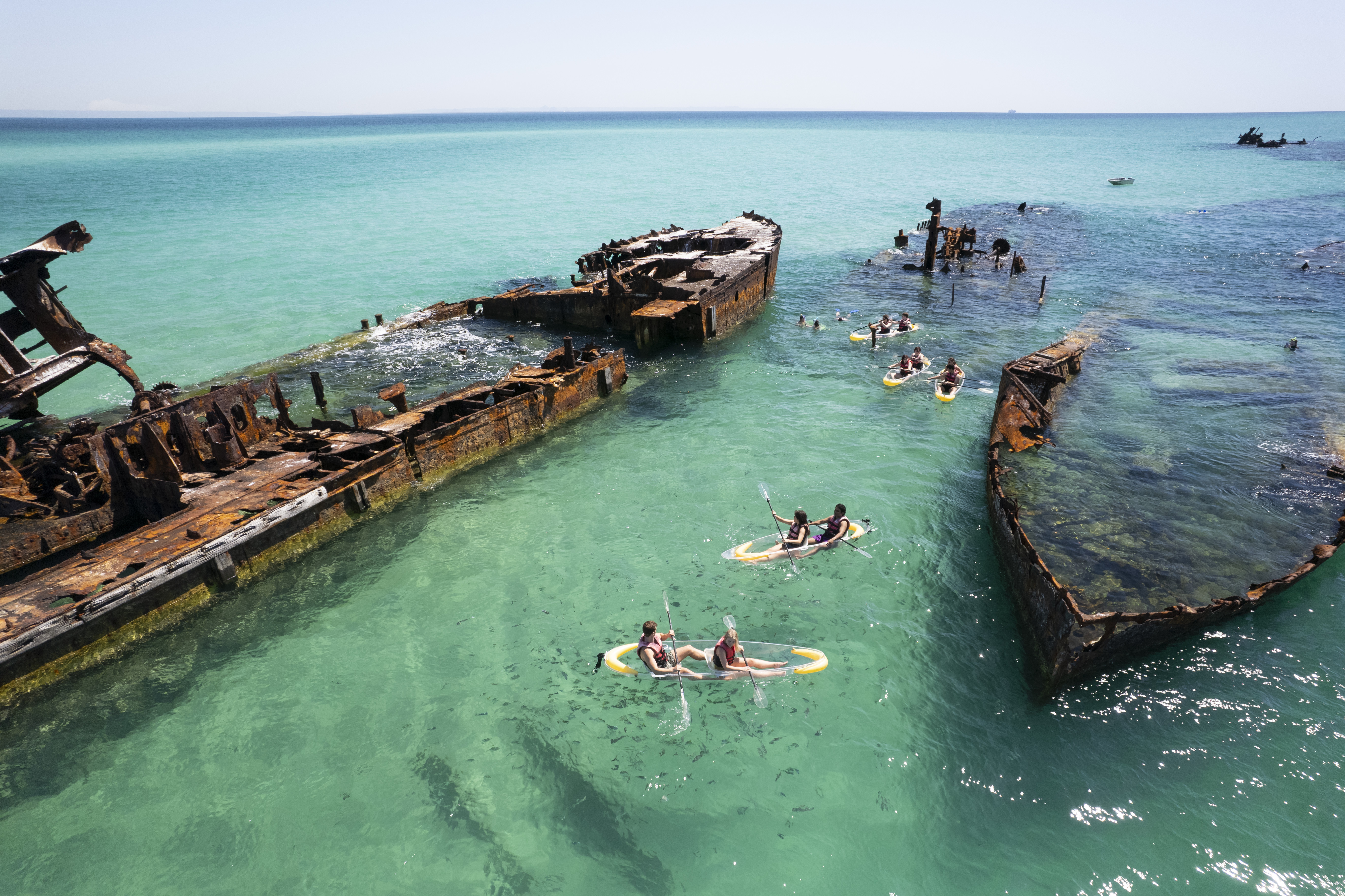 Groups of kayakers paddle between sunken vessels in the clear blue waters of Moreton Island Groups of kayakers paddle between sunken vessels in the clear blue waters of Moreton Island