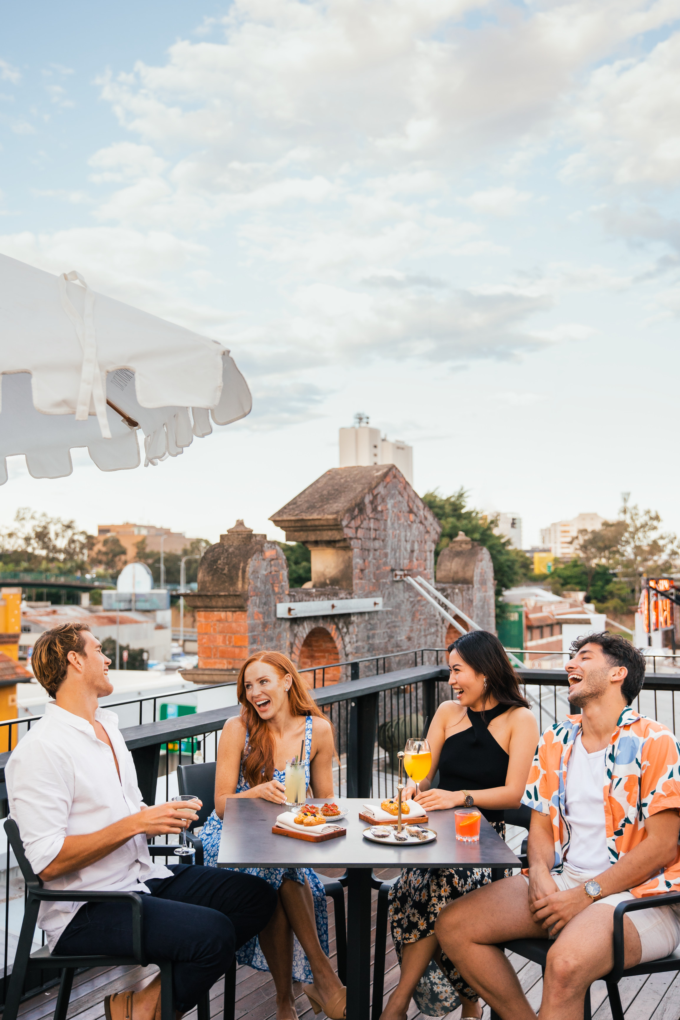 Friends laugh and sip drinks at a bar table on the rooftop of Ooh La La