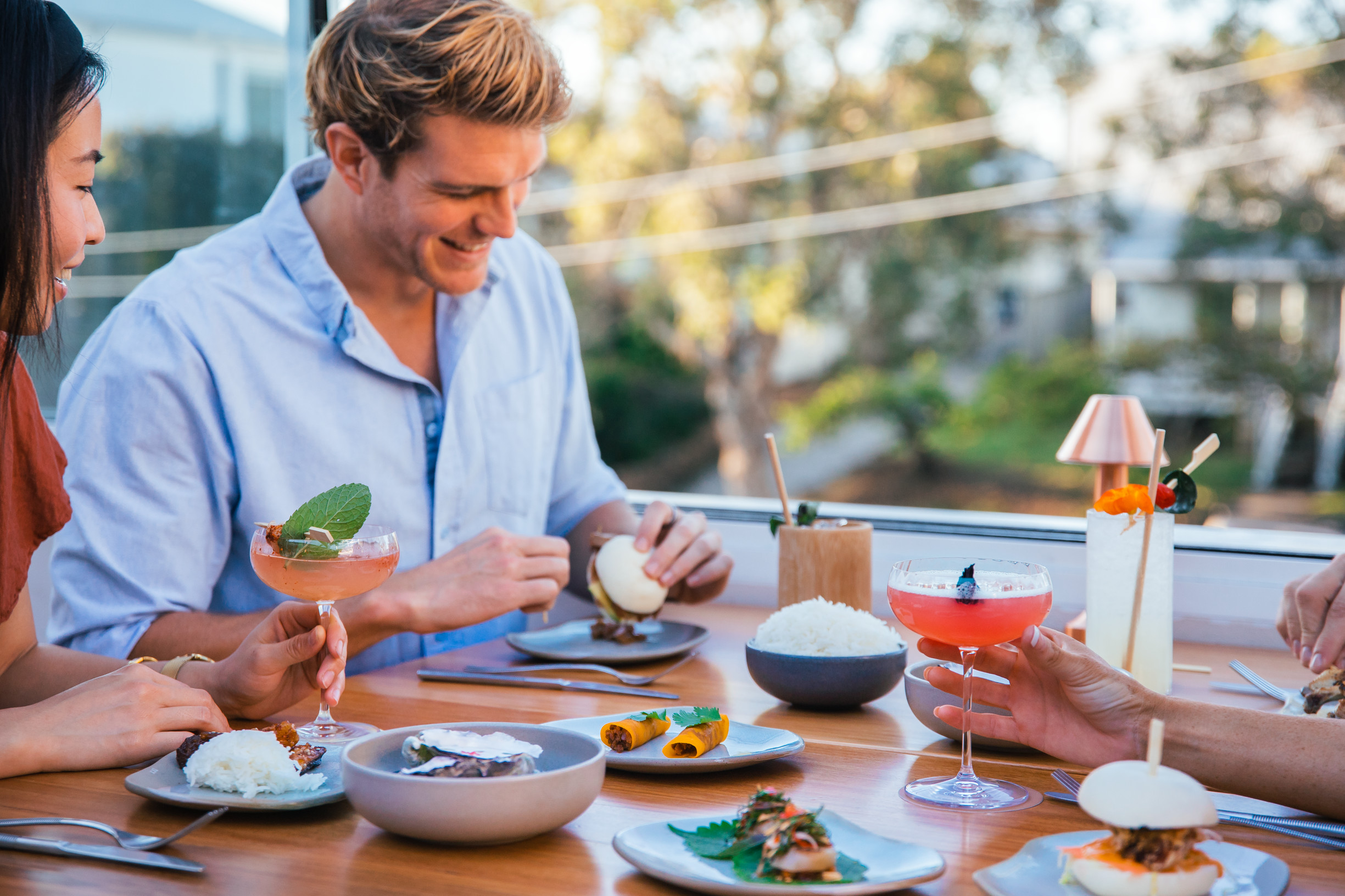 Friends sit down for dinner and cocktails at an Asian inspired rooftop bar in Brisbane suburbs
