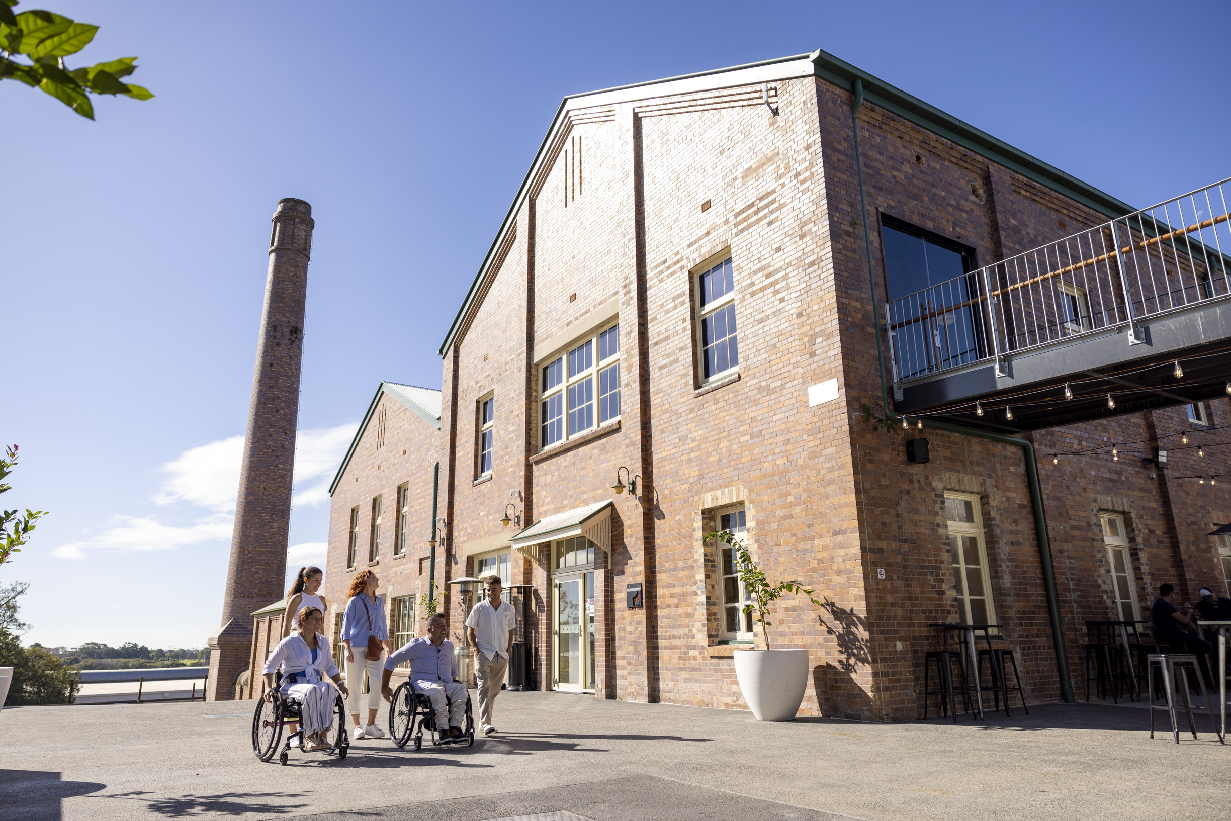 Group of five people arriving at the heritage riverside precinct, Rivermakers Brisbane. Two are in wheelchairs | accessible travel Brisbane Group of five people arriving at the heritage riverside precinct, Rivermakers Brisbane. Two are in wheelchairs | accessible travel Brisbane