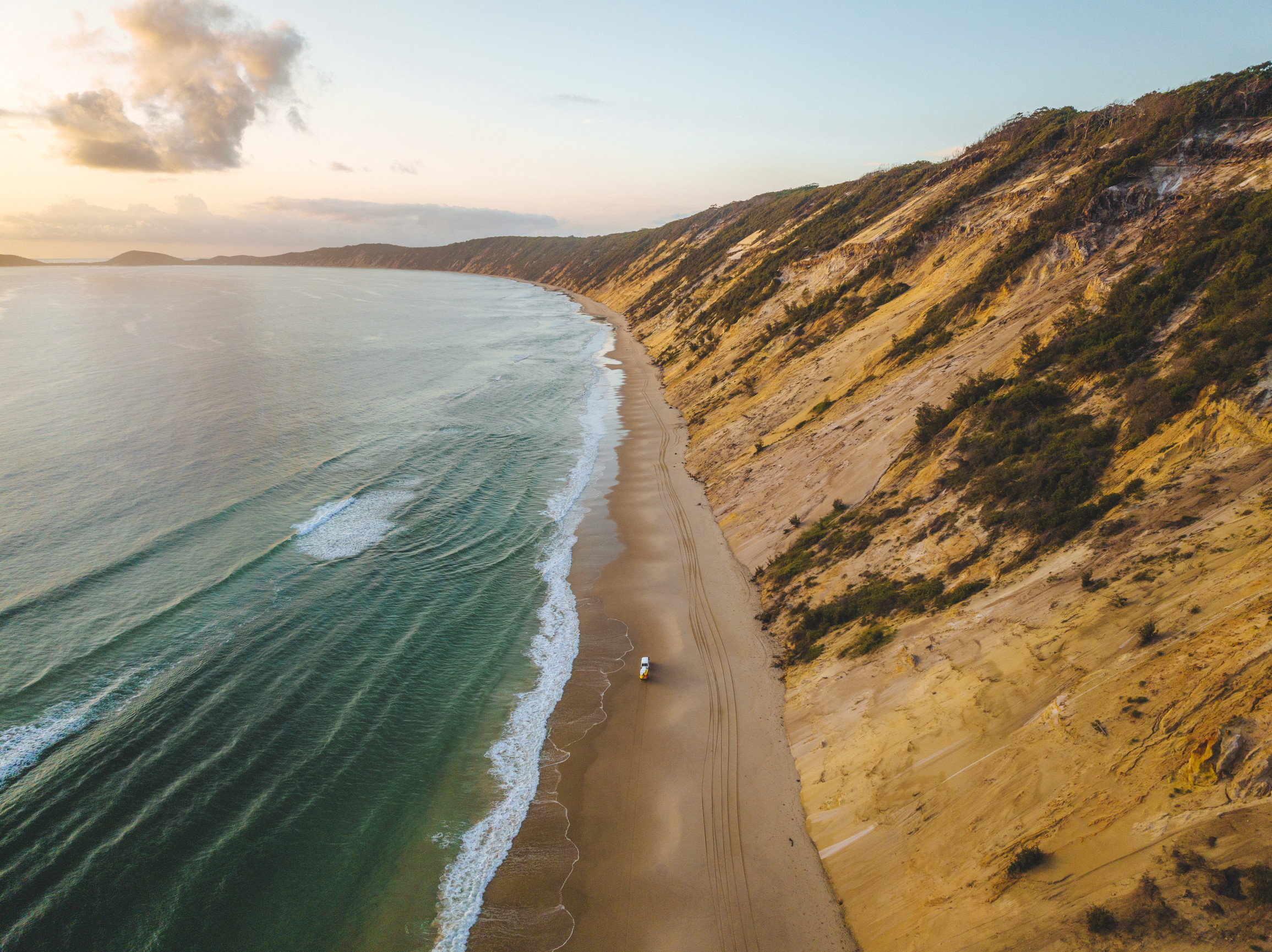 Aerial view of 4WD driving on a sandy beach, ocean on one side, sand dunes on the other Aerial view of 4WD driving on a sandy beach, ocean on one side, sand dunes on the other