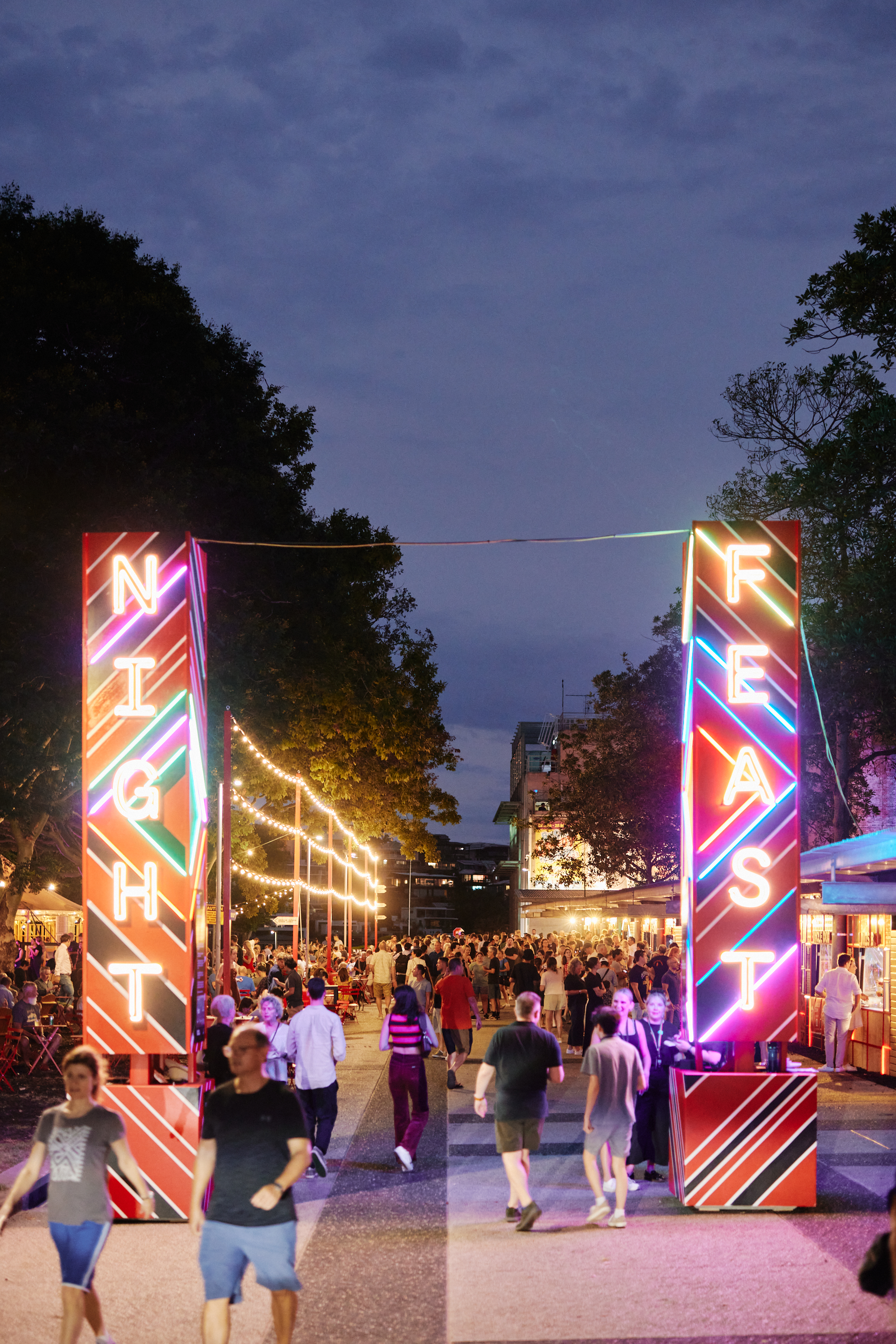 A group of people walk along the neon-lit walkway of Night Feast