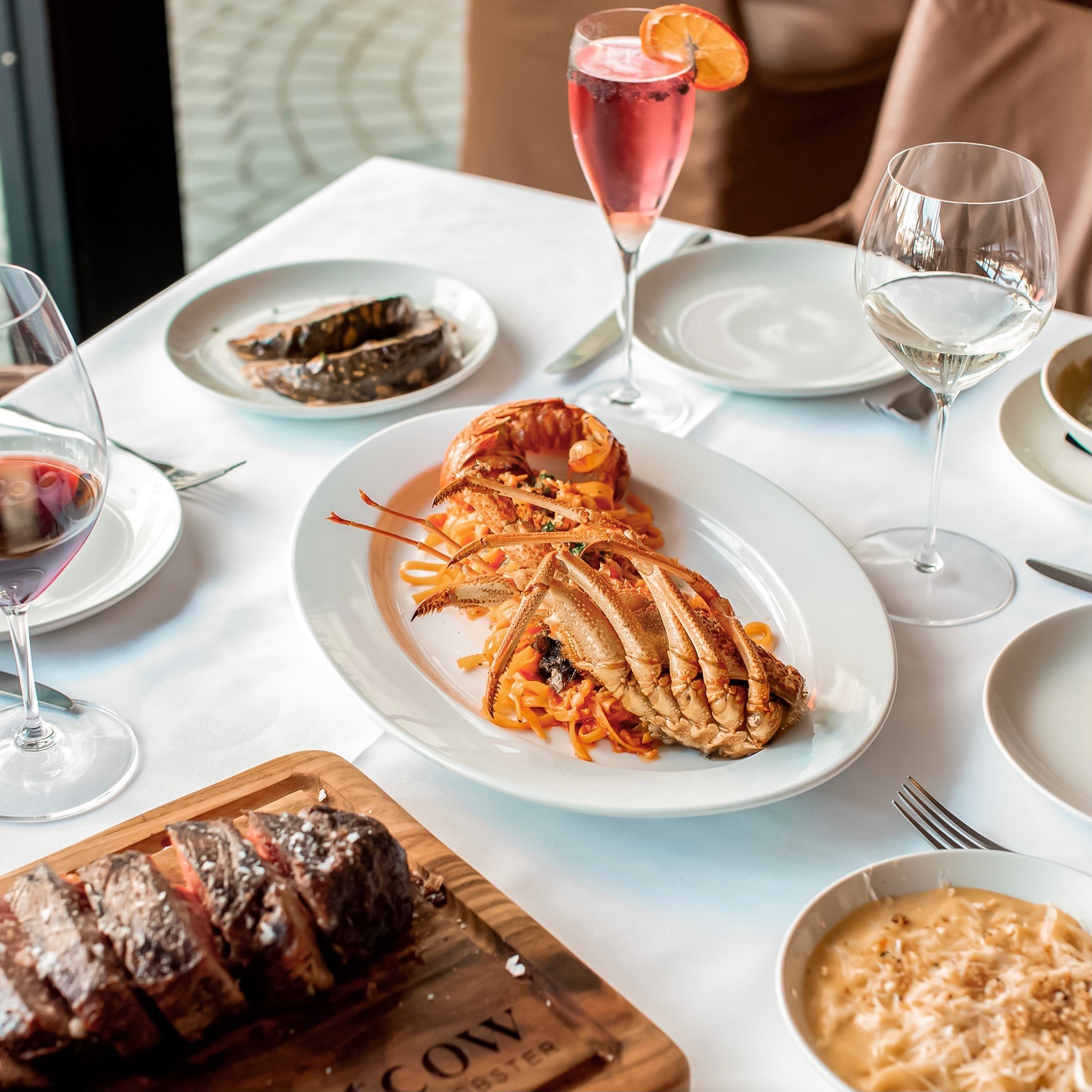 Lobster, steak and sides are served on a table at Fatcow, Fortitude Valley, along with a glass of wine and pink champagne Lobster, steak and sides are served on a table at Fatcow, Fortitude Valley, along with a glass of wine and pink champagne