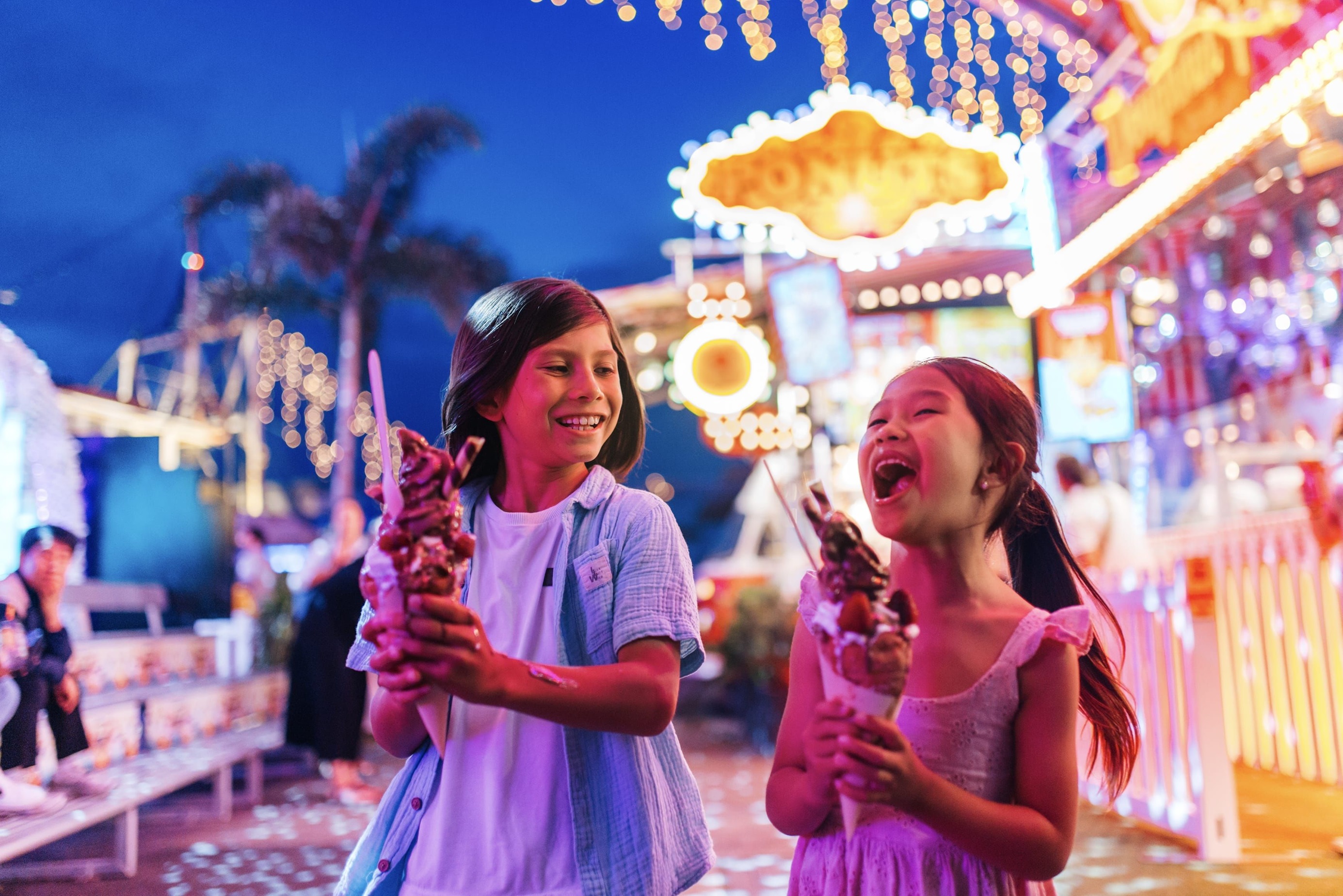 Young boy and girl walk through a night food market holding giant ice creams