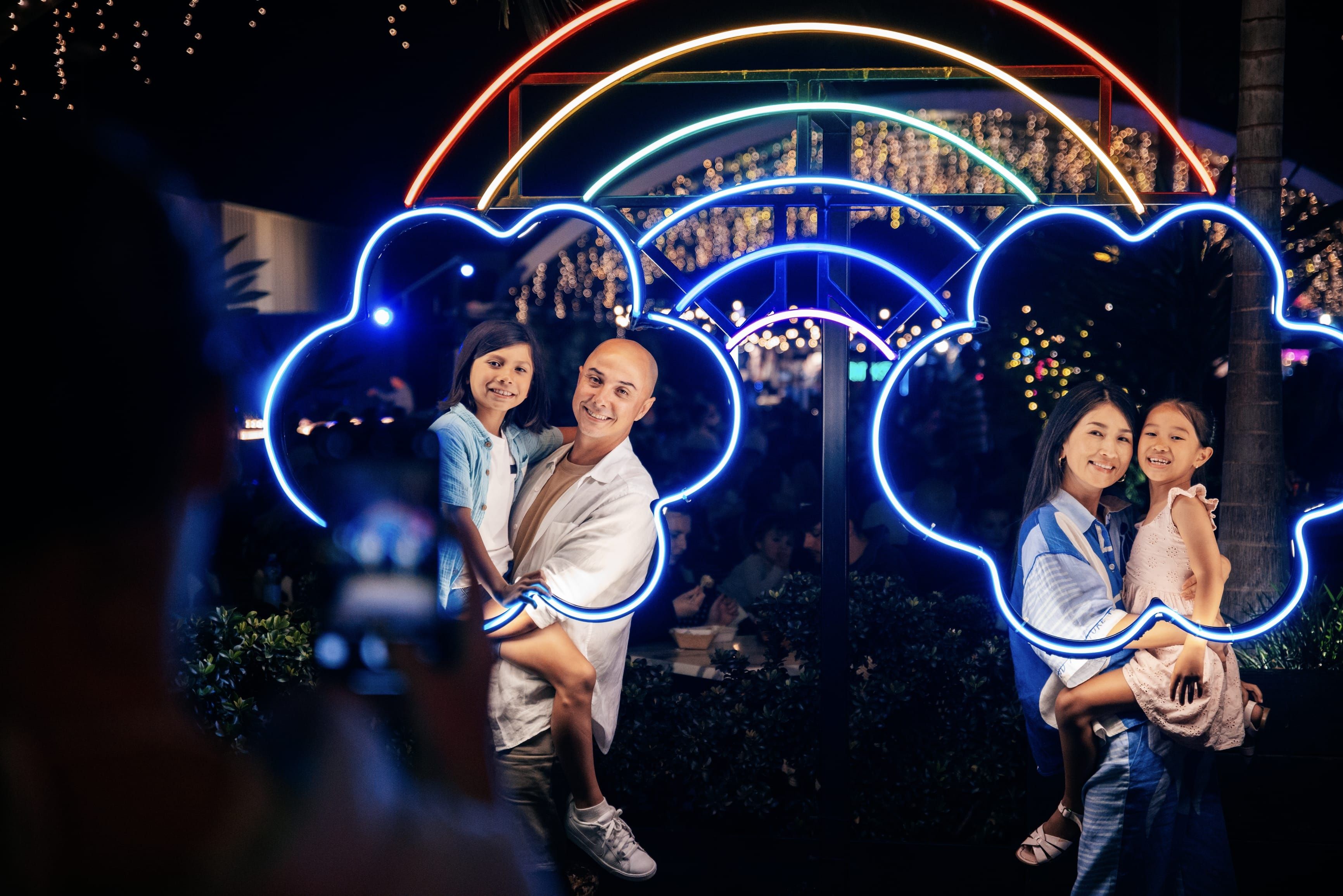 Family pose for photos among neon light artworks at a night market