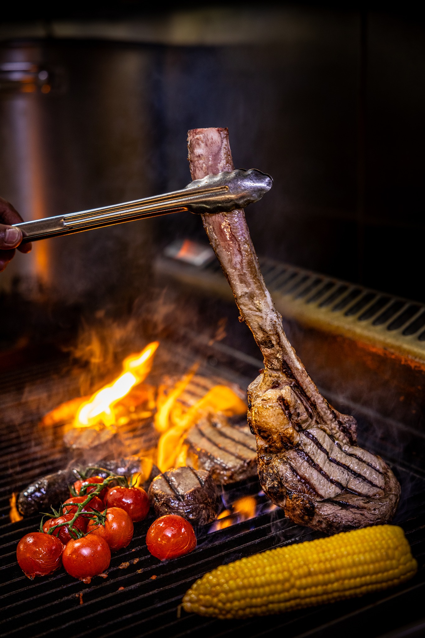 Argentinian steaks cooking on fire of a parilla grill, with corn and tomatoes at Calida South Bank Argentinian steaks cooking on fire of a parilla grill, with corn and tomatoes at Calida South Bank