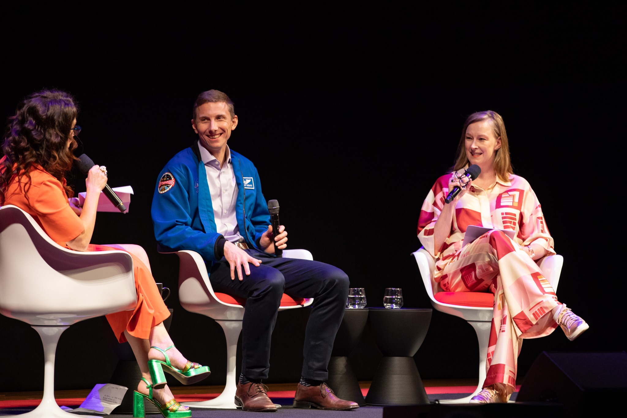 Three people sit on stage for a panel discussion Three people sit on stage for a panel discussion