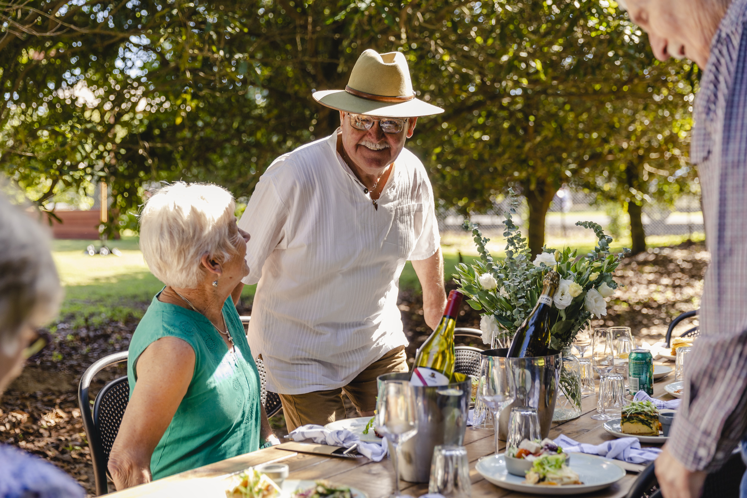 Group of mature aged friends enjoying lunch among the trees at Macadamias Australia, where there is an immersive visitor experience to learn about the history and process of macadamia farming in Bundaberg Group of mature aged friends enjoying lunch among the trees at Macadamias Australia, where there is an immersive visitor experience to learn about the history and process of macadamia farming in Bundaberg