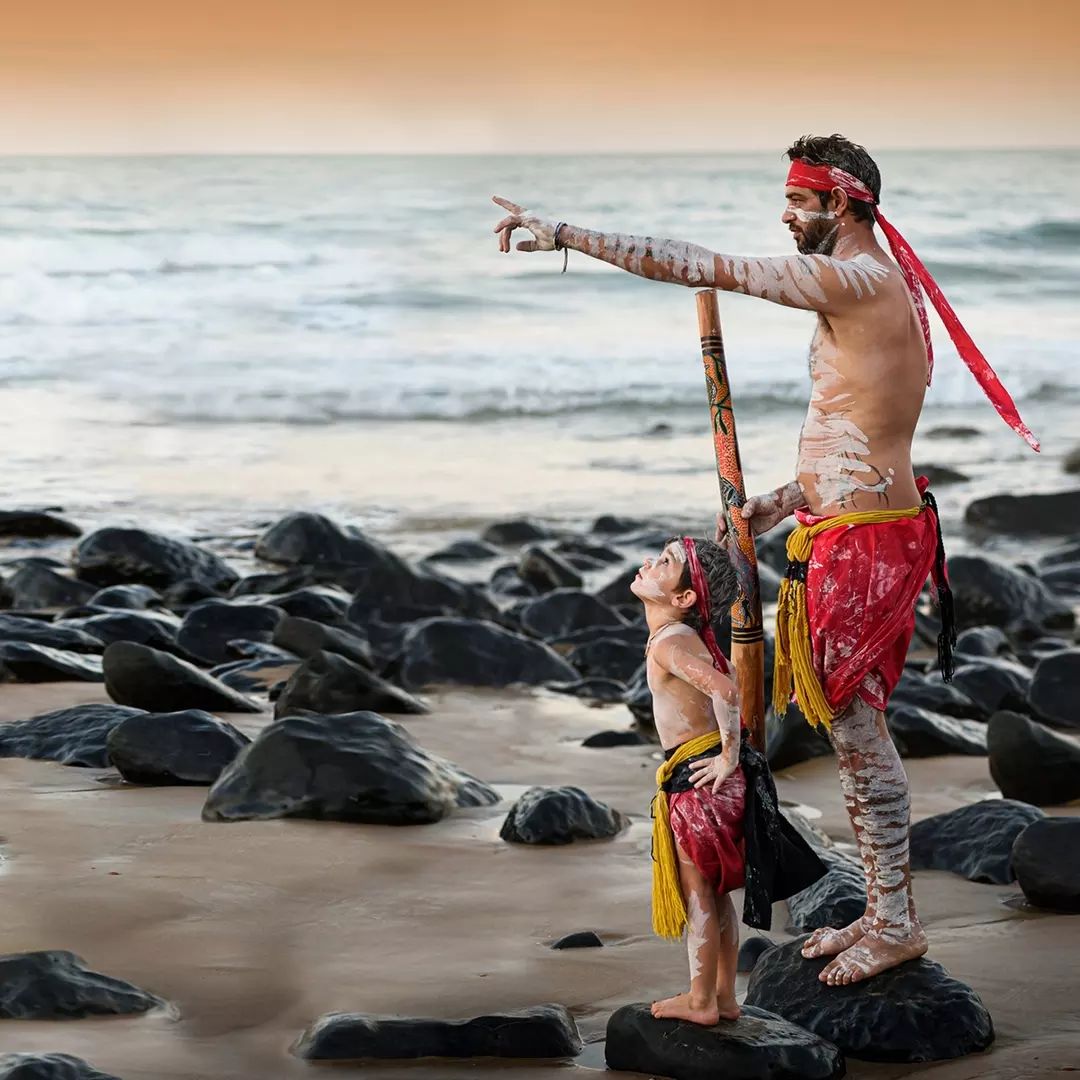 Aboriginal boy and man stand in traditional dress on the beach during Milbi Festival, Bundaberg Aboriginal boy and man stand in traditional dress on the beach during Milbi Festival, Bundaberg