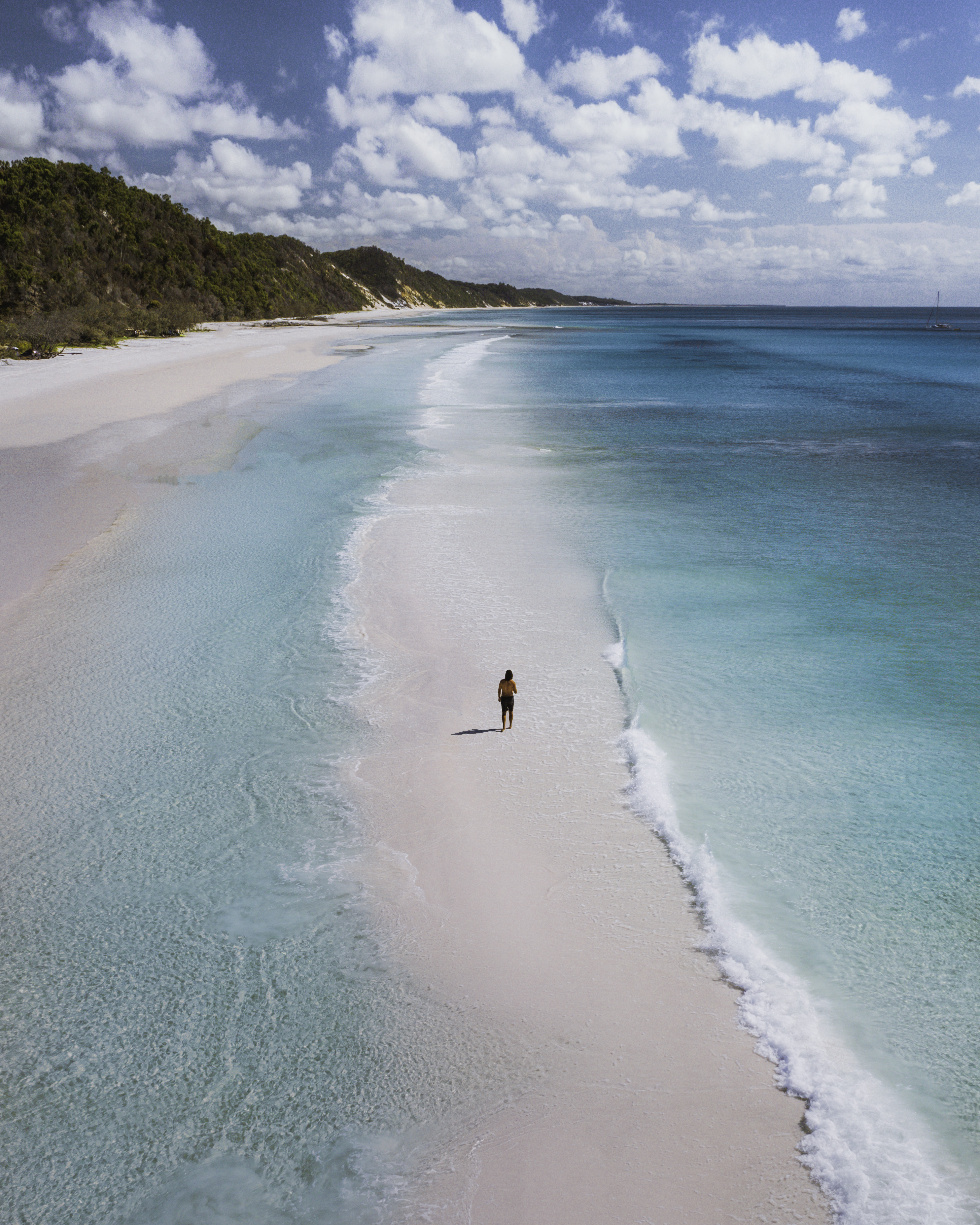 Man walks along white sand beach between two stretches of pristine blue water