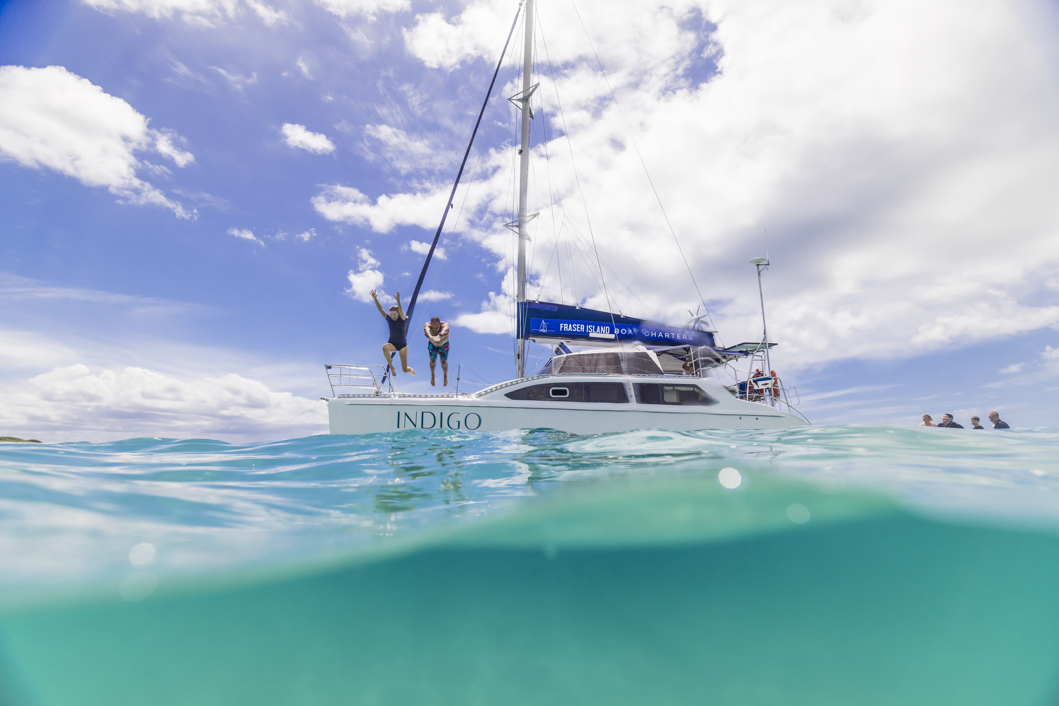 Two people dive off a sailing yacht into blue waters Two people dive off a sailing yacht into blue waters