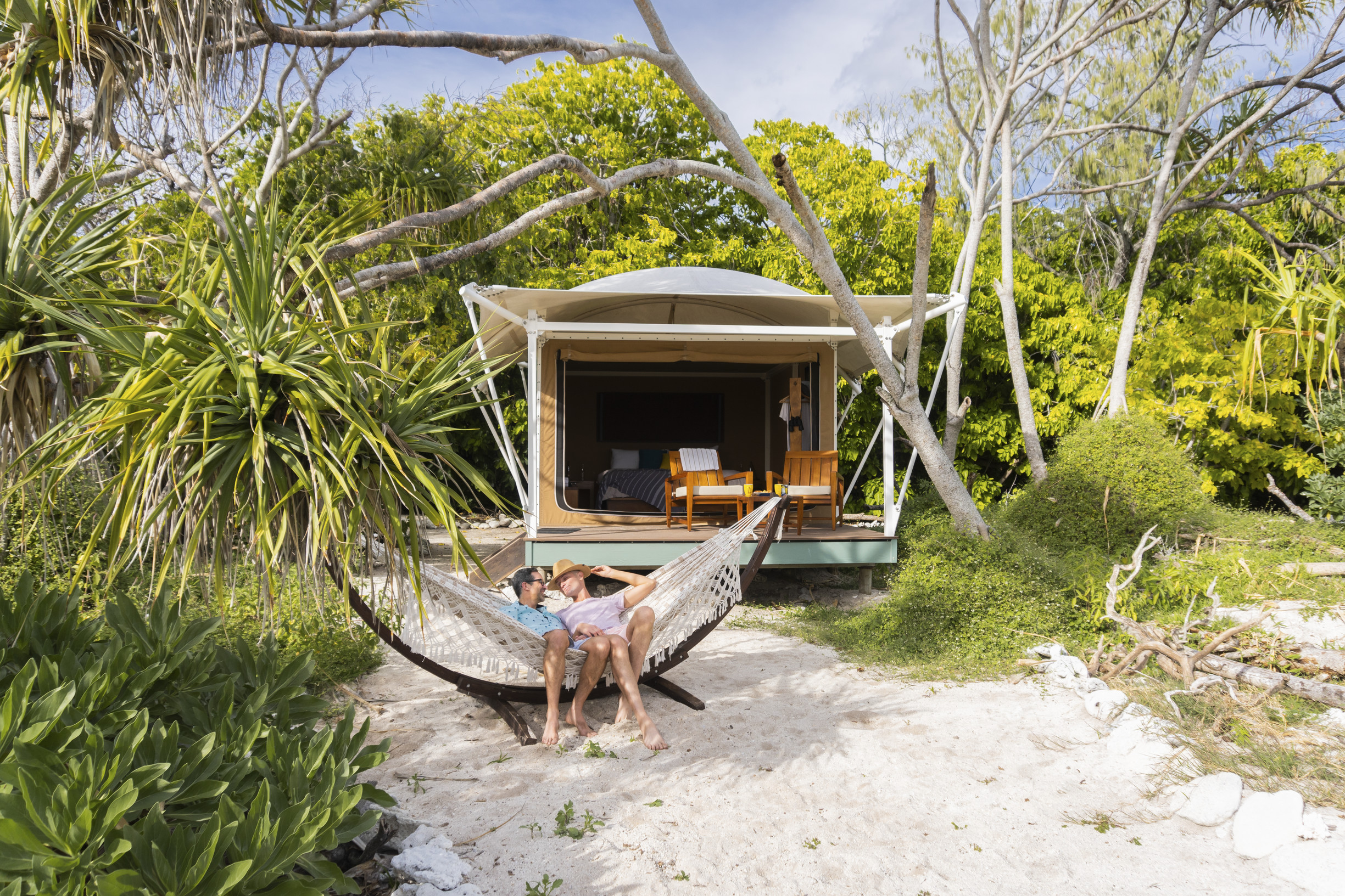 Couple relaxing in a hammock in front of their beachfront glamping tent