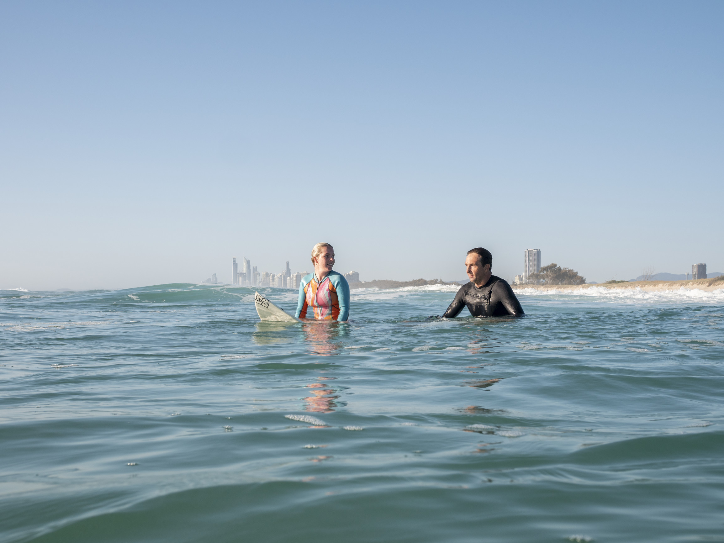 Surfers in the water with the Gold Coast skyline behind them