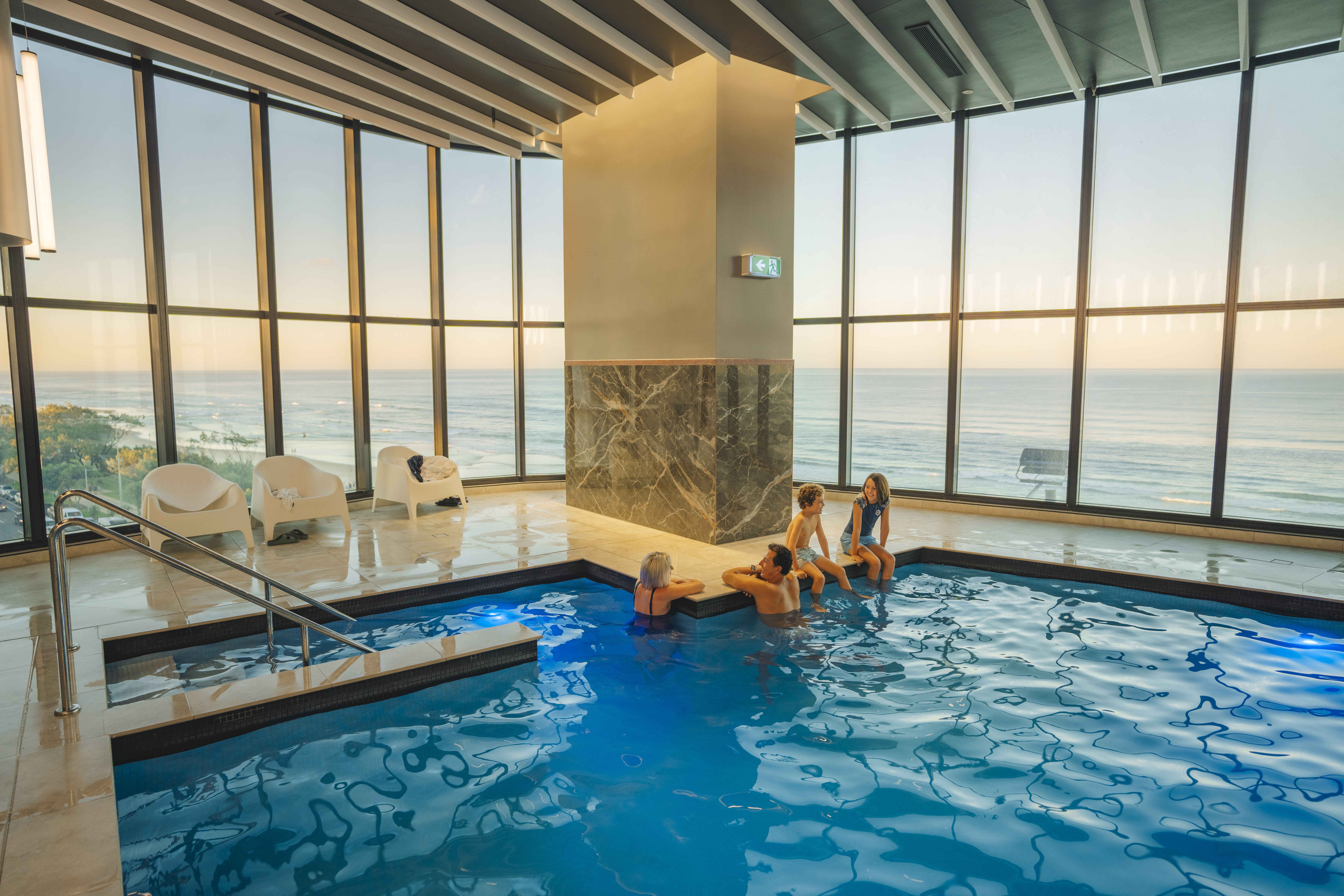 Family of four relax in indoor pool with Gold Coast beach and ocean views