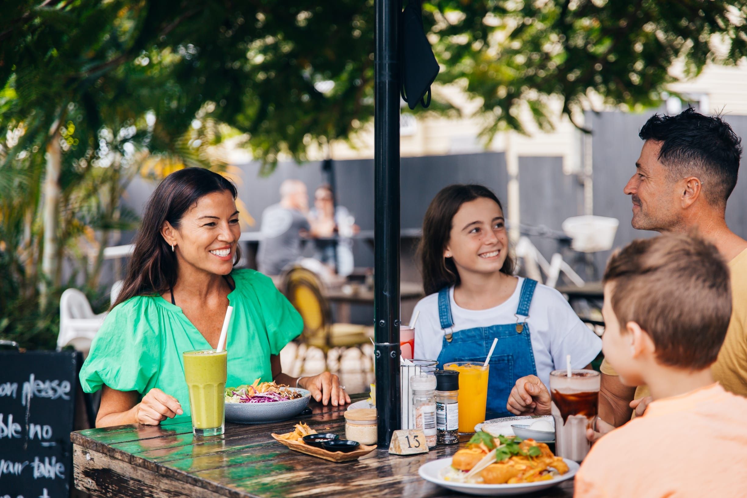 Family enjoying breakfast in the cafe garden at Stones Throw Cafe, Currumbin Family enjoying breakfast in the cafe garden at Stones Throw Cafe, Currumbin