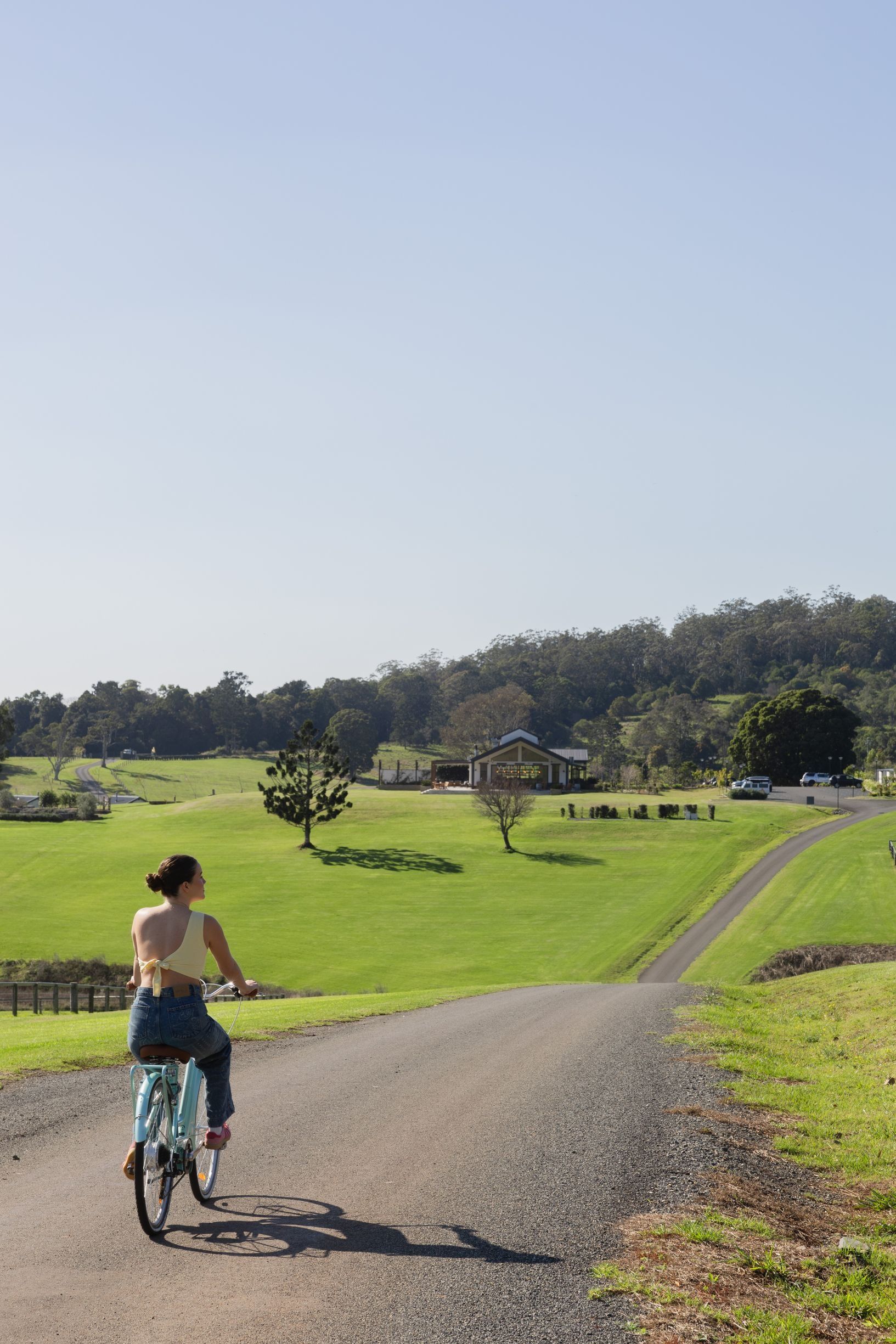 Woman rides bicycle along country road surrounded by rolling green hills