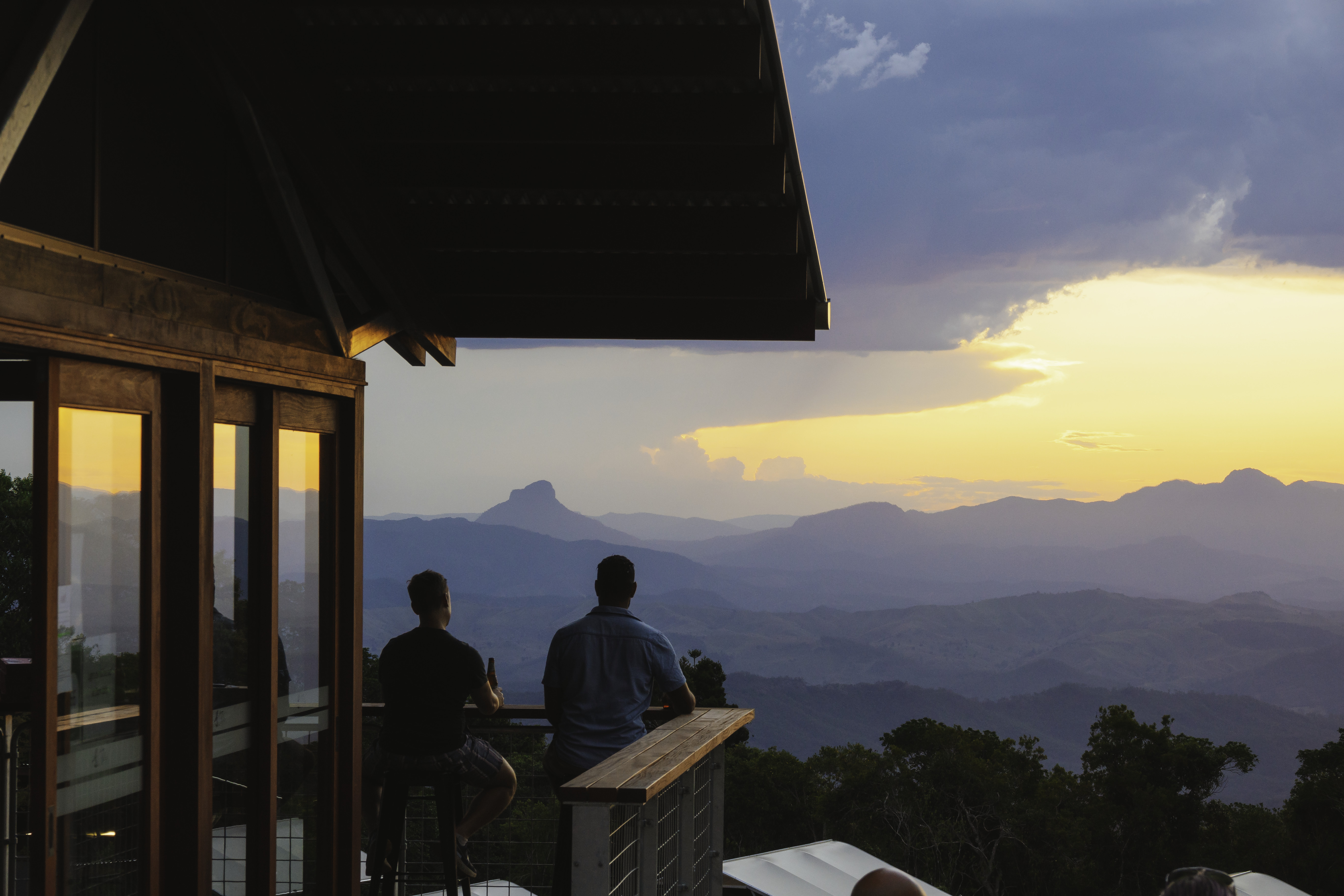 Two men enjoy a drink on the balcony of a campers lodge overlooking mountain range