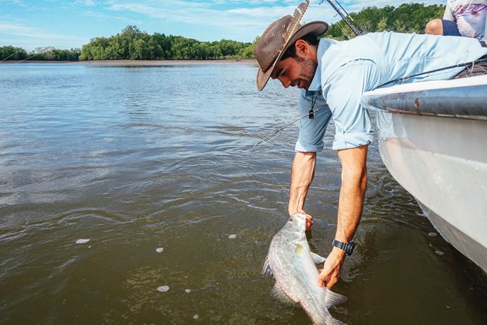 Man pulls fish from water while fishing from a boat at Pioneer River, Mackay
