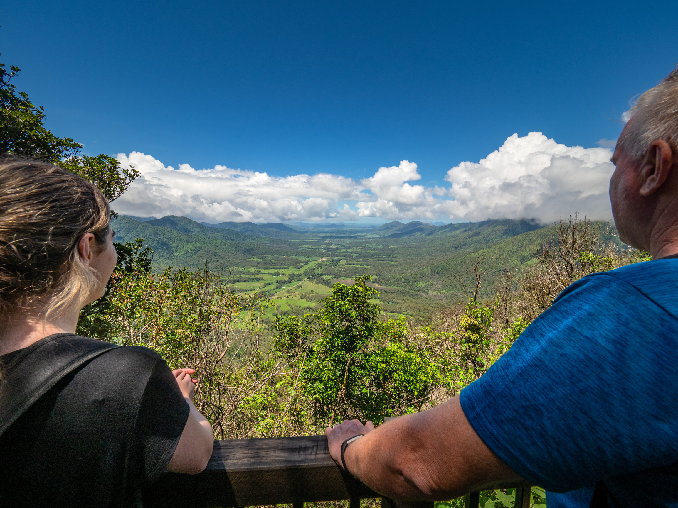 two hikers take in mountain range views from a lookout two hikers take in mountain range views from a lookout