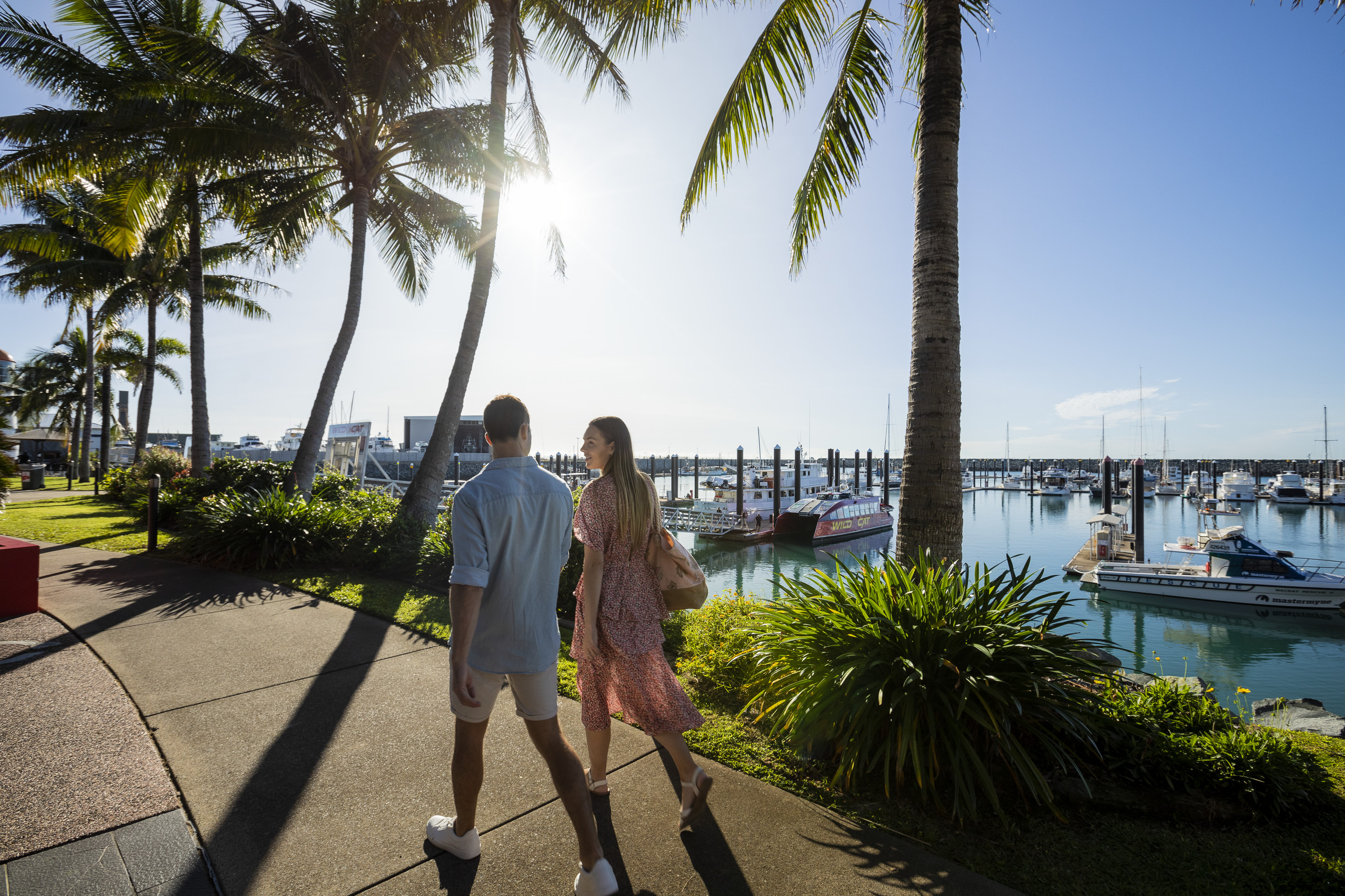 Couple walking along wide footpaths at Mackay Harbour, with boats in the background Couple walking along wide footpaths at Mackay Harbour, with boats in the background