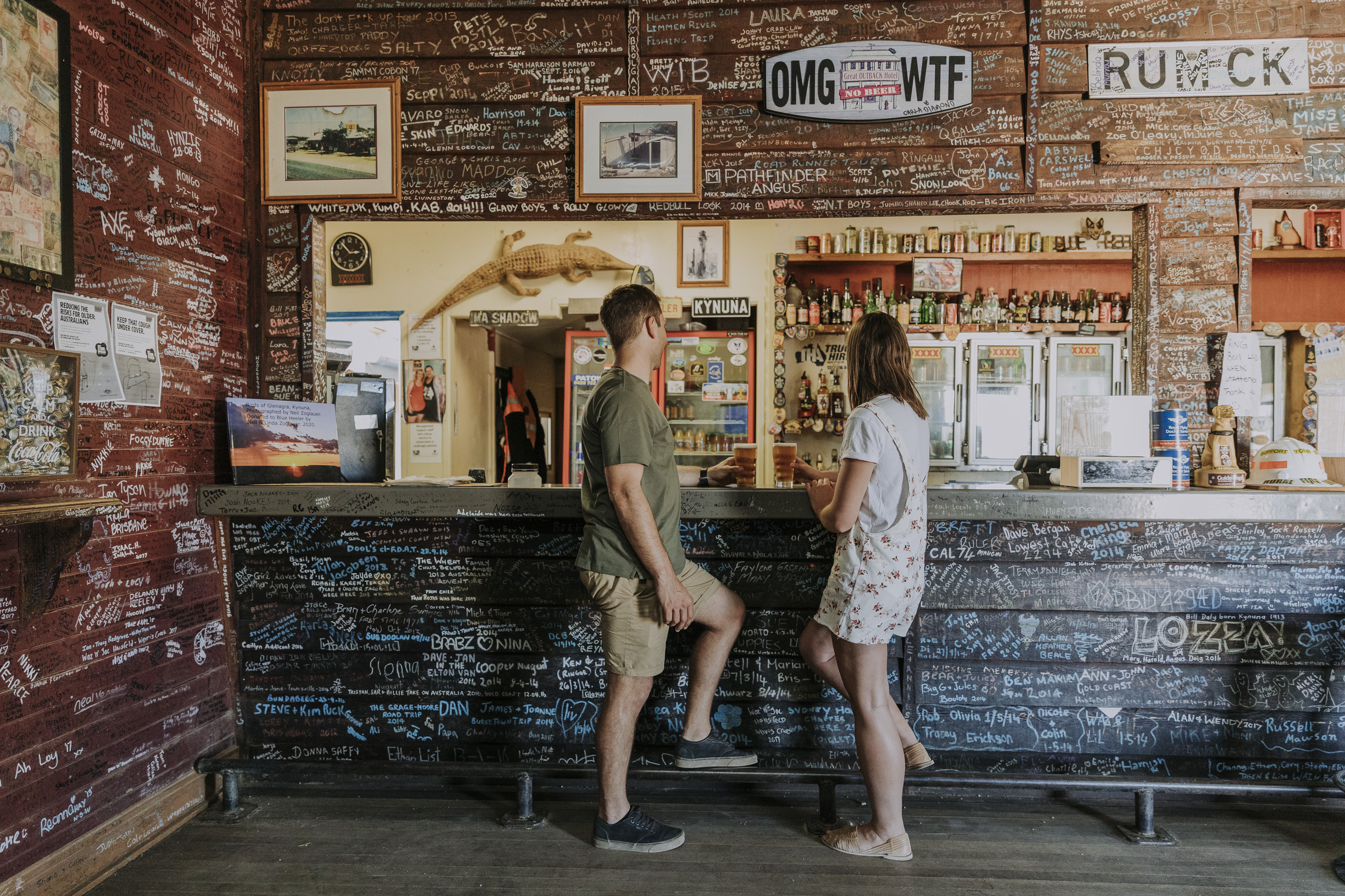 Man and woman hold beers and stand at the bar of The Blue Heeler Hotel, Kynuna
