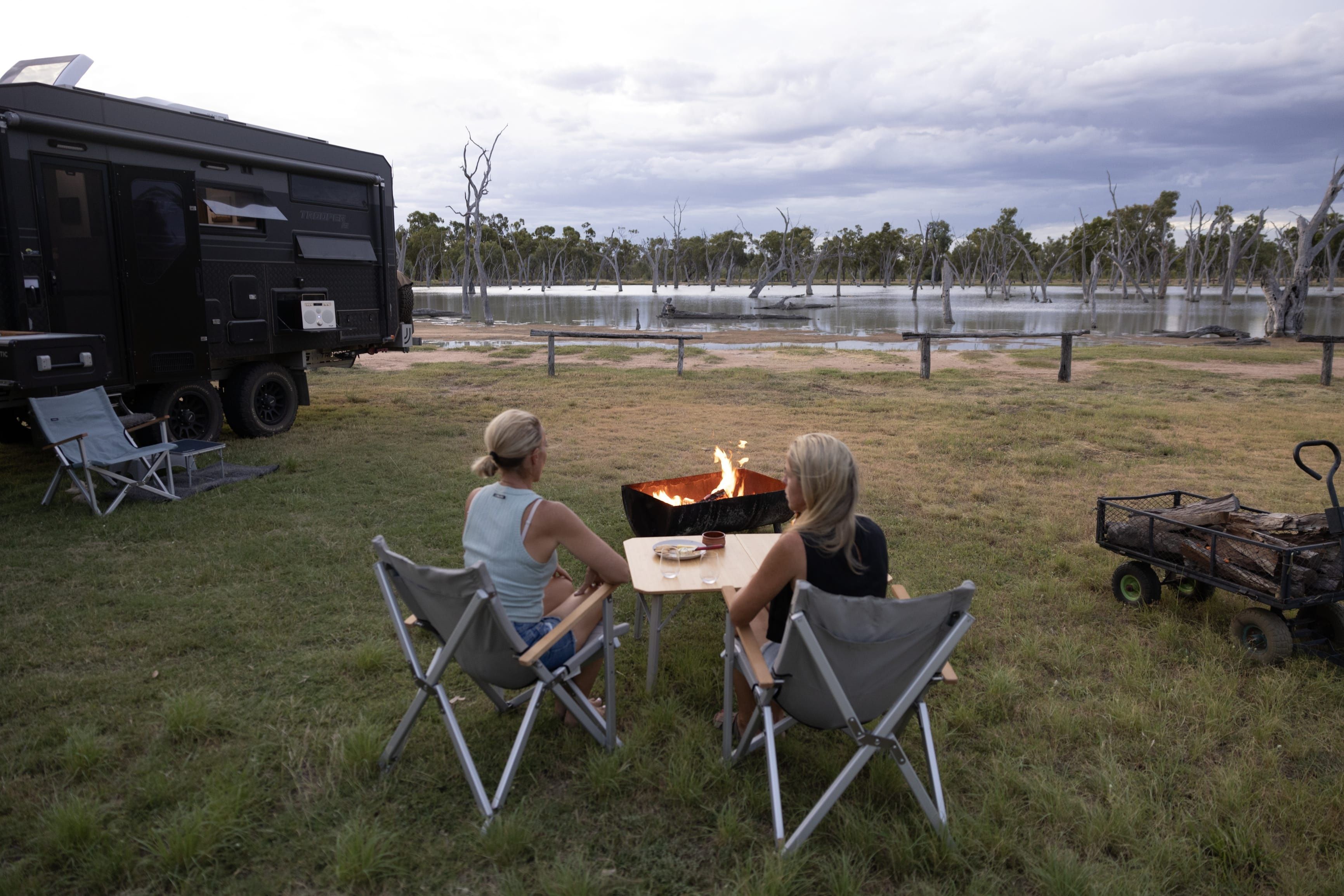 Two women relax by the campfire at Lara Wetlands Station, bush camping accommdation set around a tranquil wetland with natural hot springs.