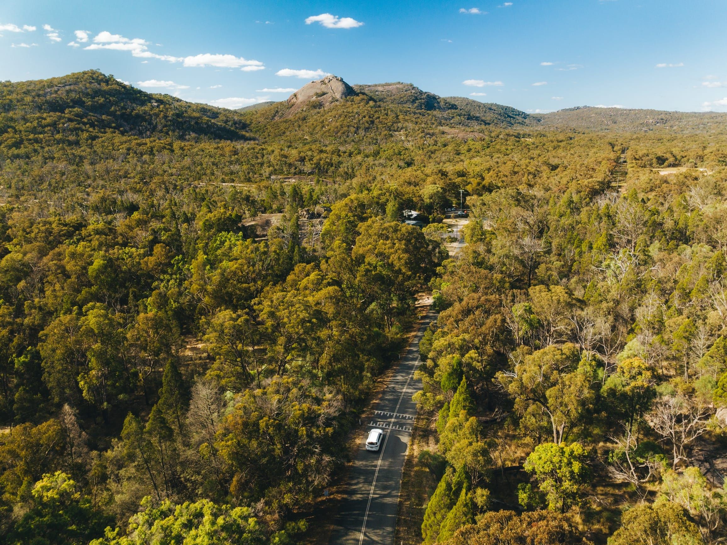 Car driving through a national park with views of bushland and rocky outcrops