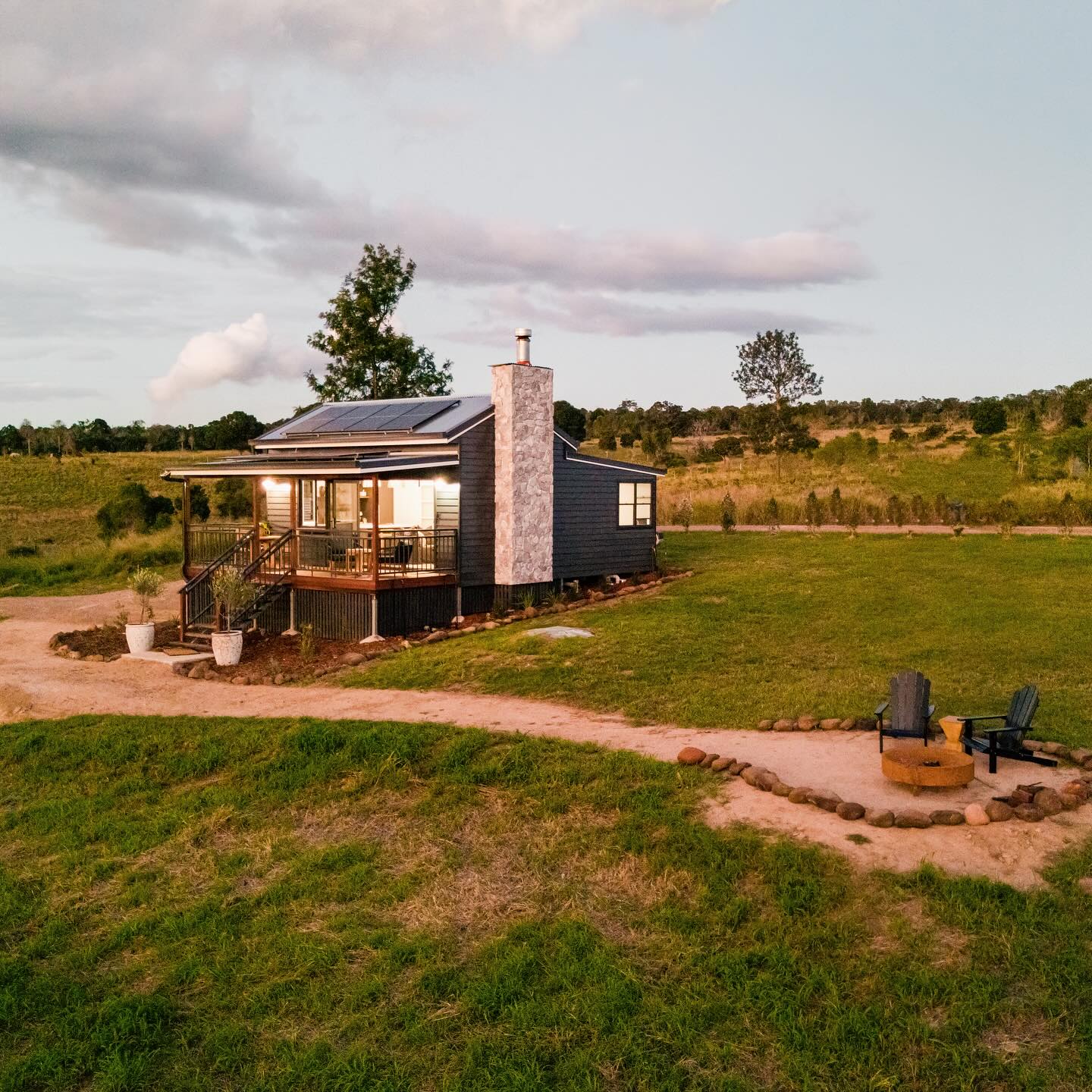 Rustic cottage stands among rolling hills, with a firepit and two chairs outside cabin at The Firebreak