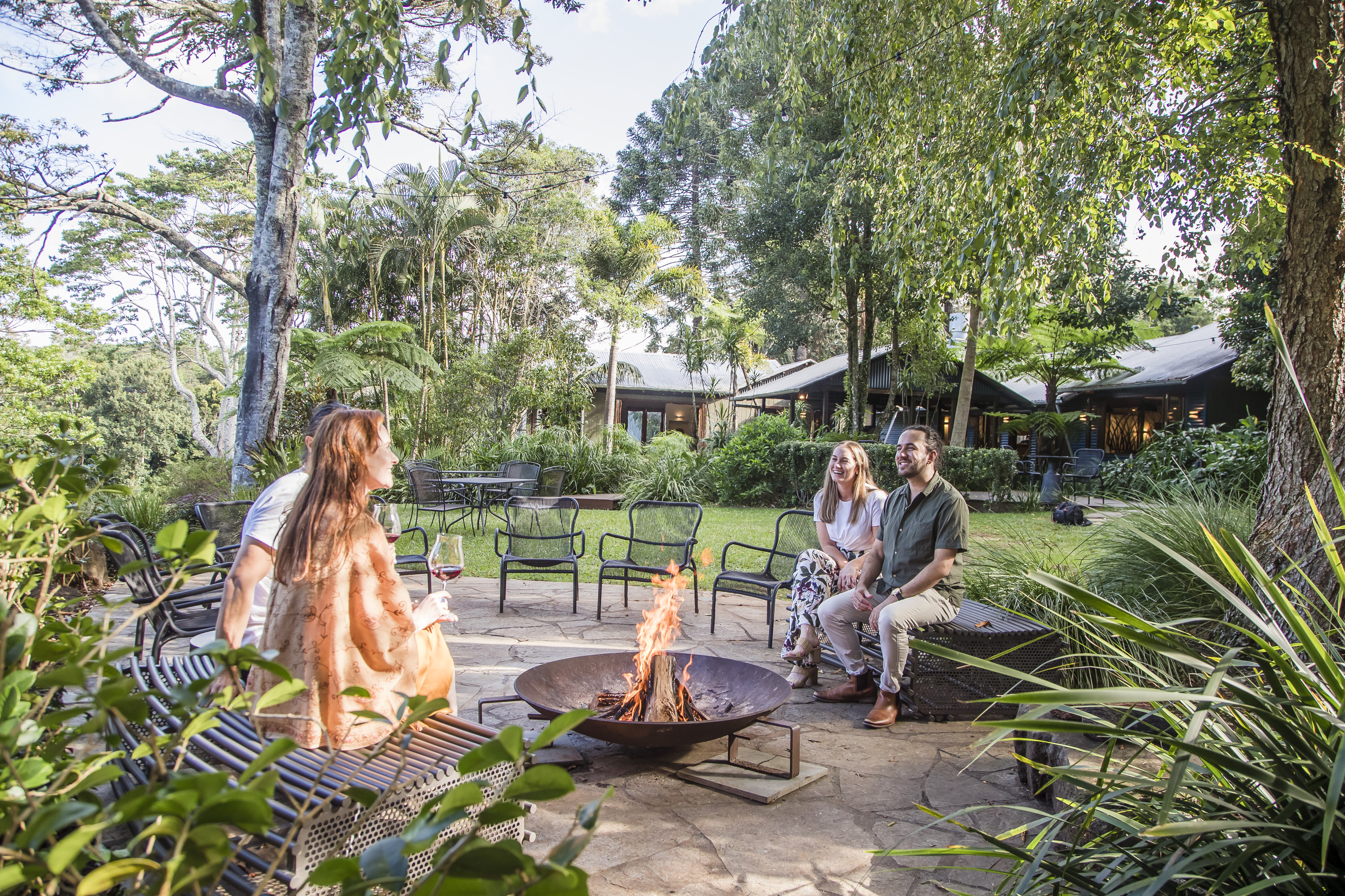 Couple relax on a bench beside open firepit surrounded by nature and fairy lights