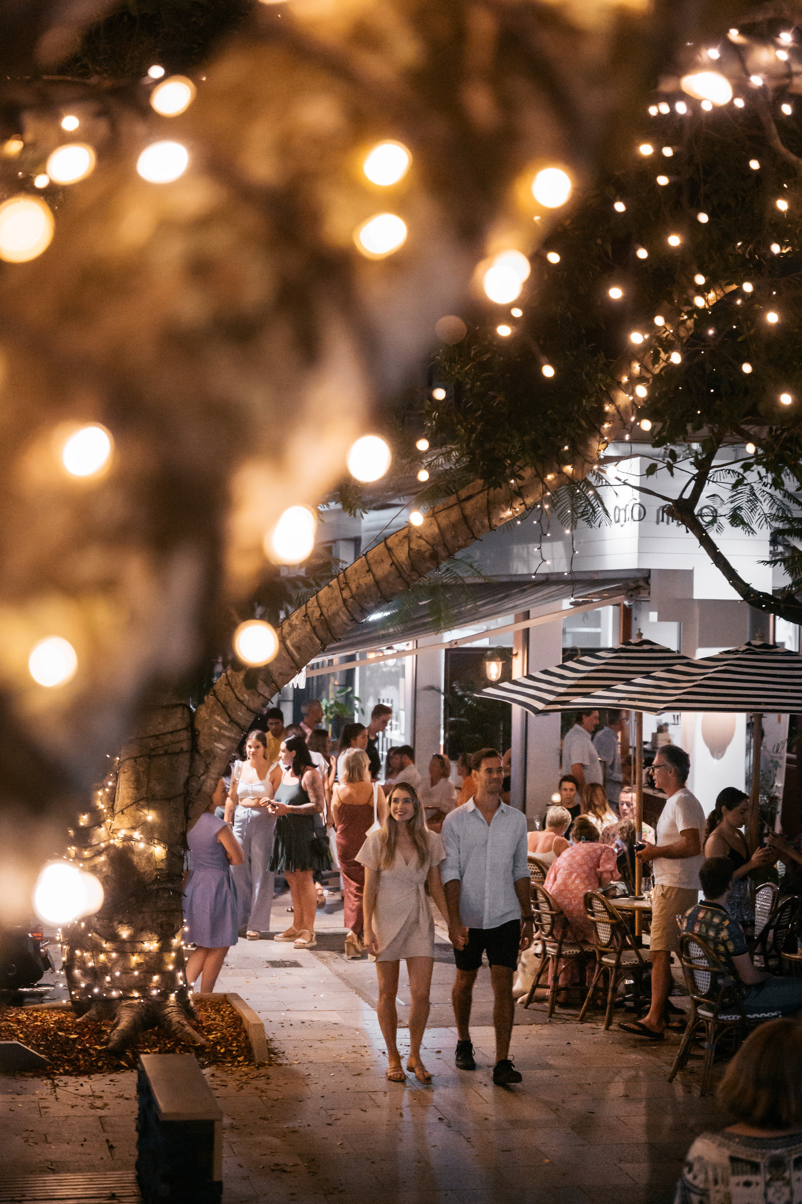 Couple walking down Hastings Street Noosa at night, illuminated by fairy lights