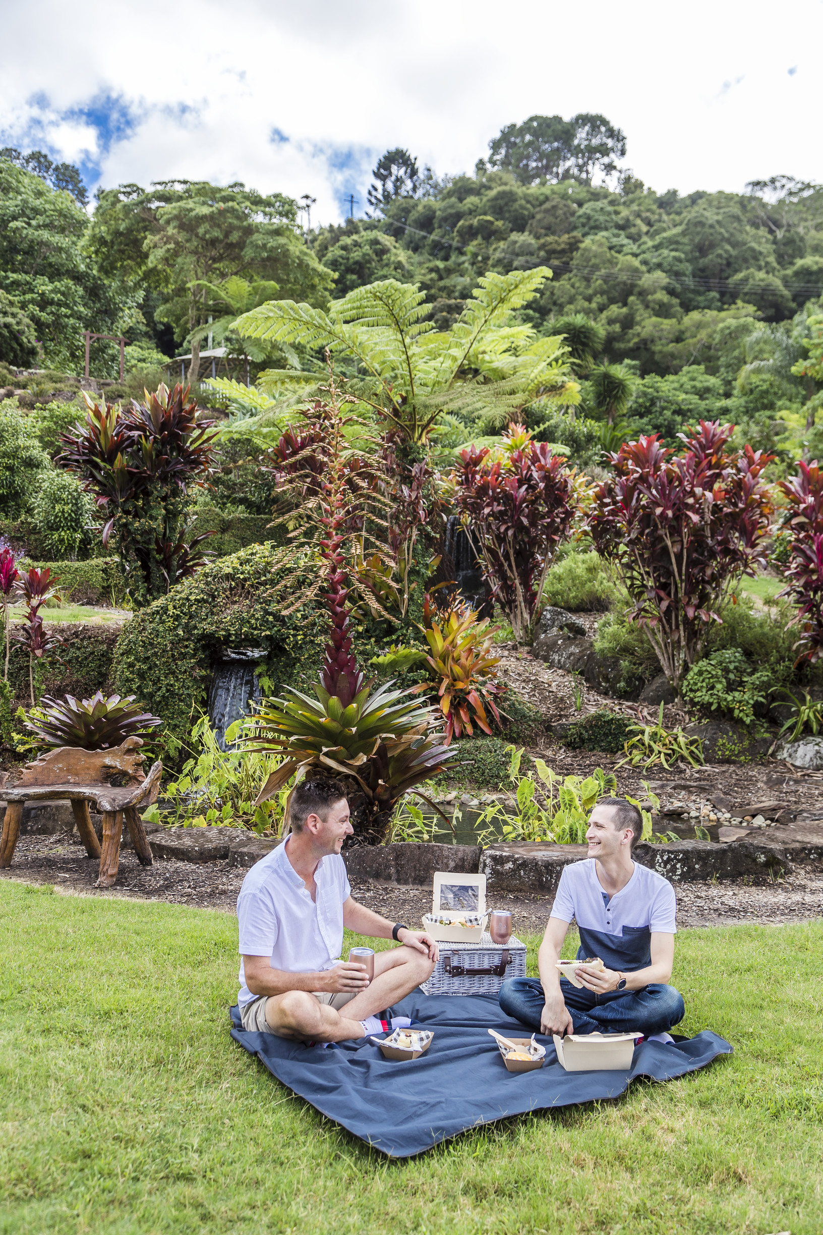 Two men enjoy a picnic among lush tropical gardens