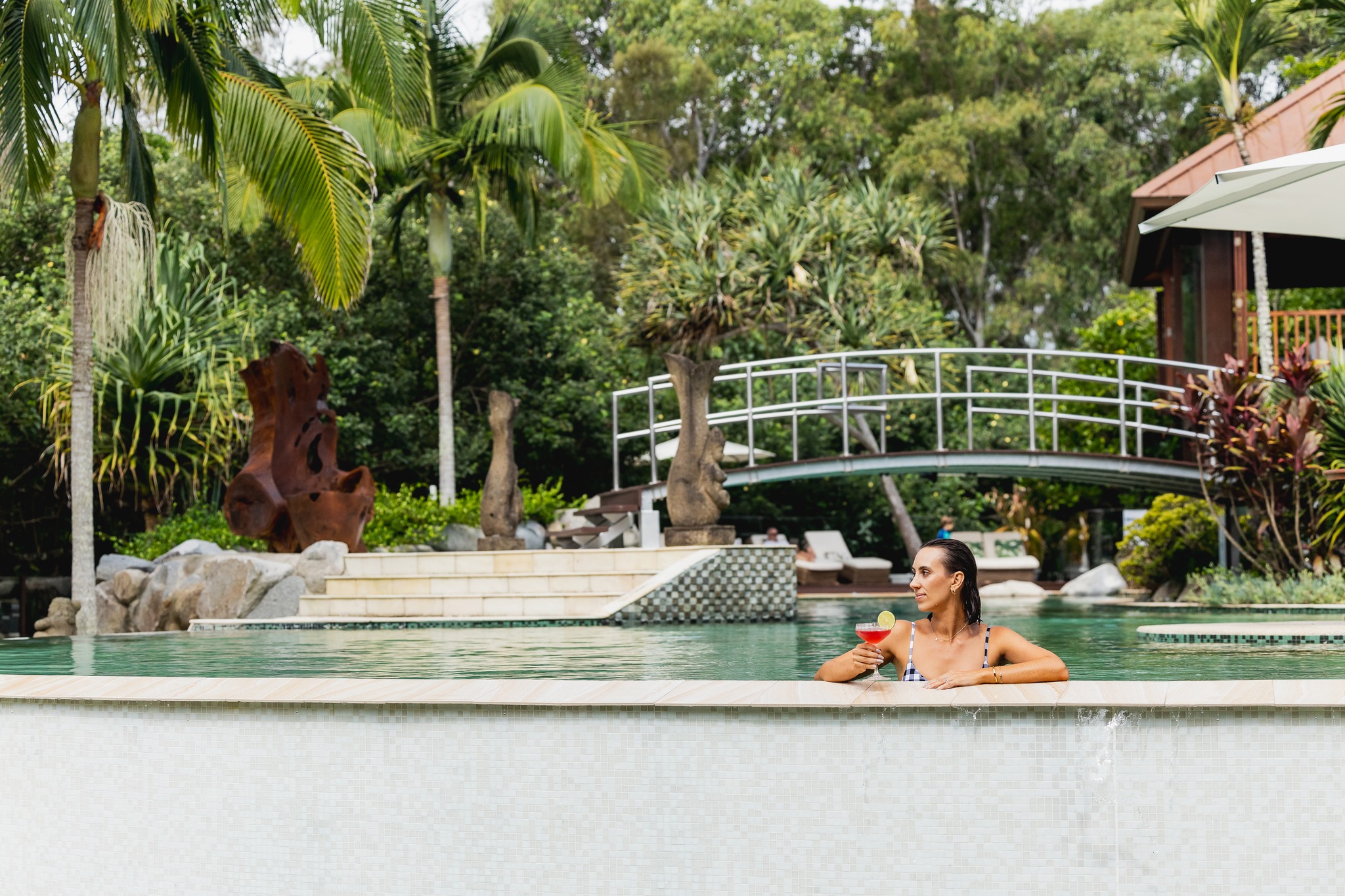 Woman rests at the edge of a pool with cocktail in hand, surrounded by tropical trees at Makepeace Island