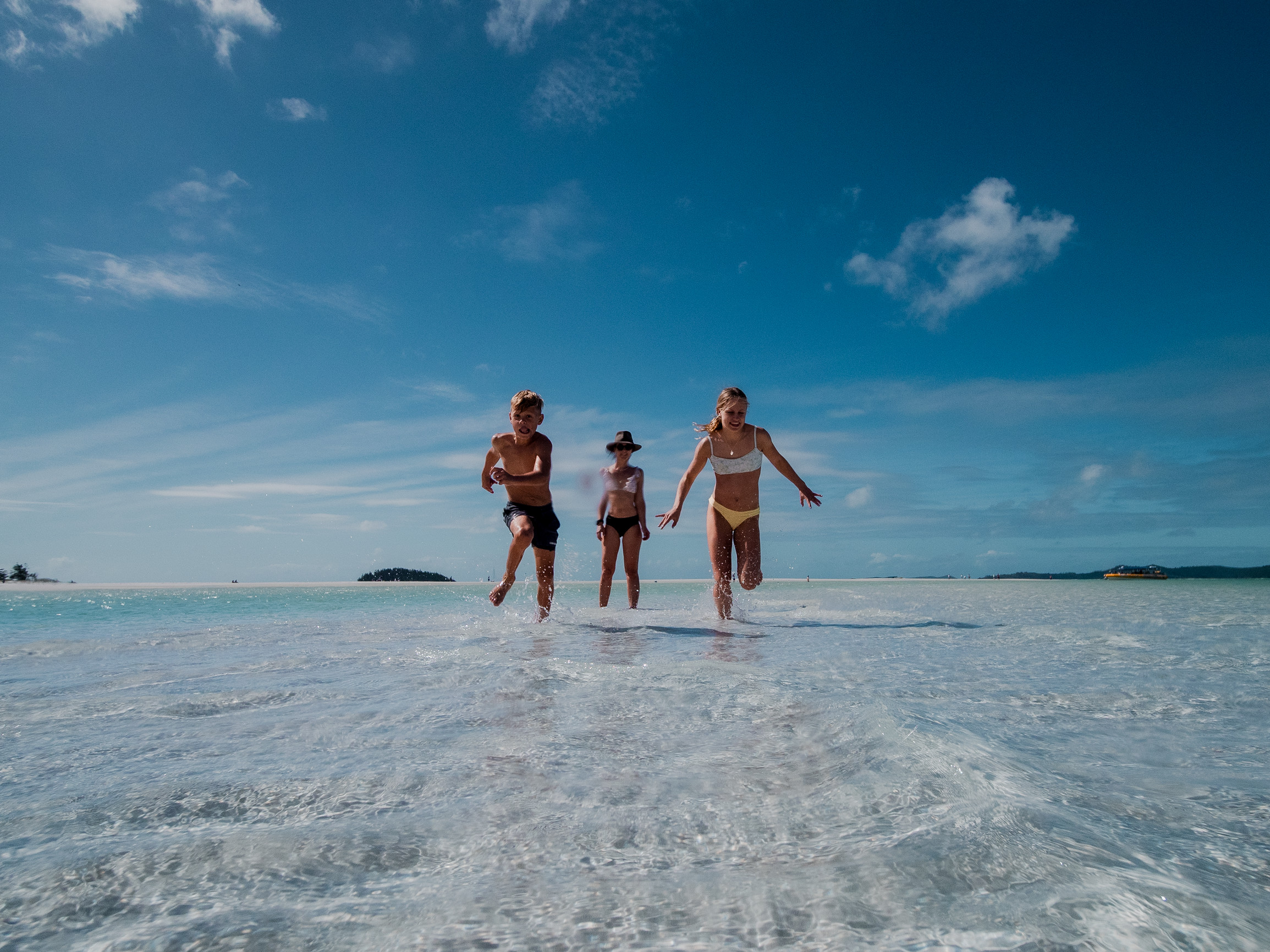 two teens and parent run through clear shallow waters of Whitehaven Beach