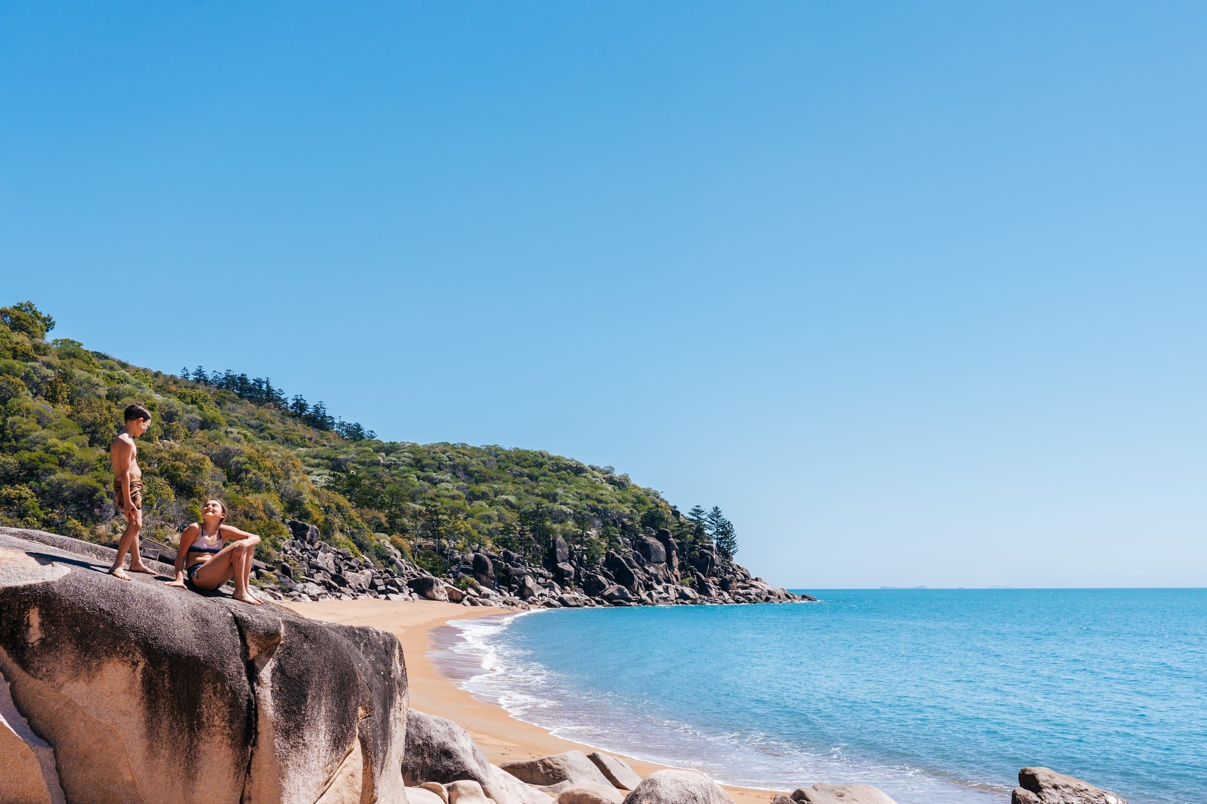 Two children play on large rocks at Nelly Bay, while on tour with Aquascene Magnetic Island