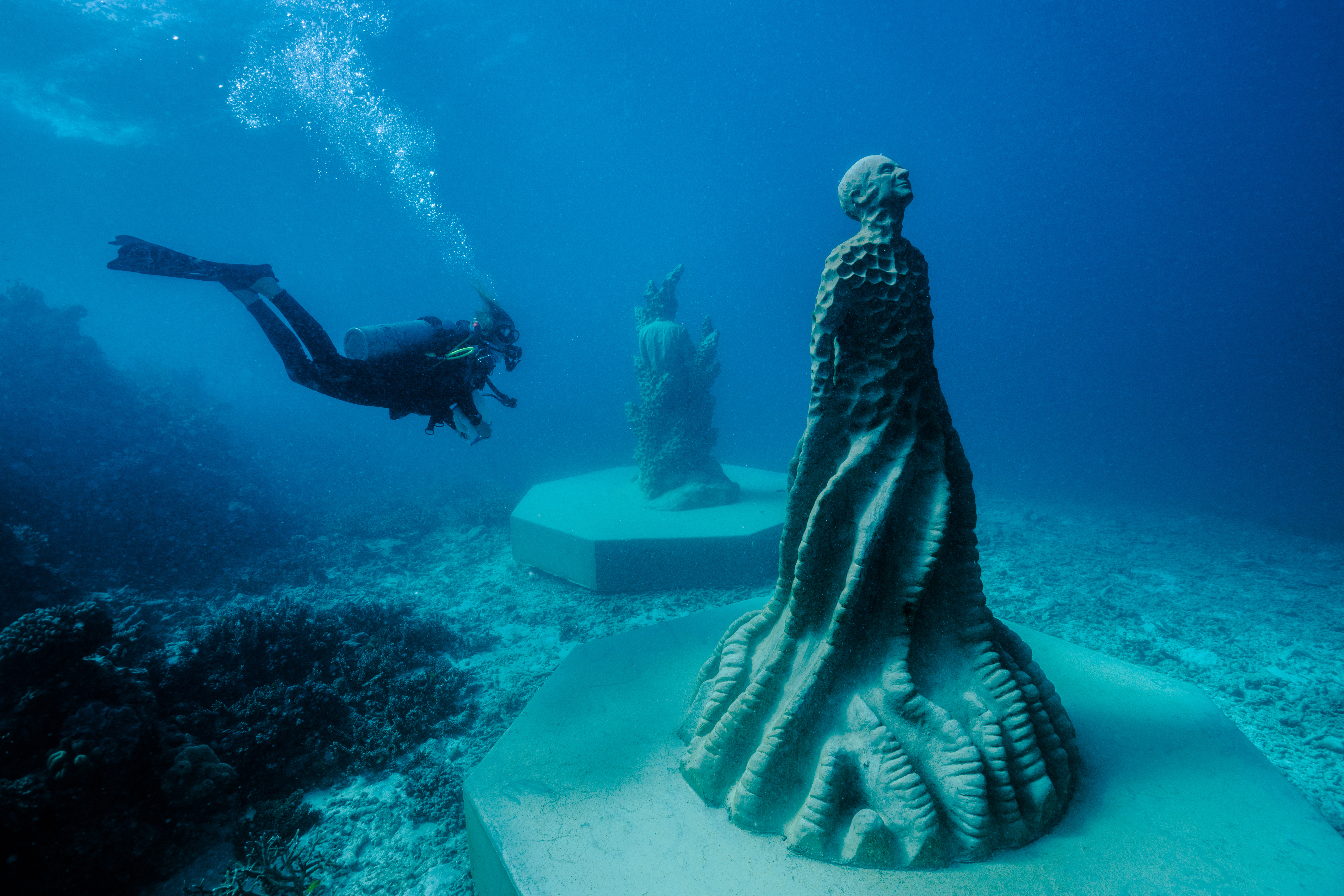 A diver underwater looking at a sculpture