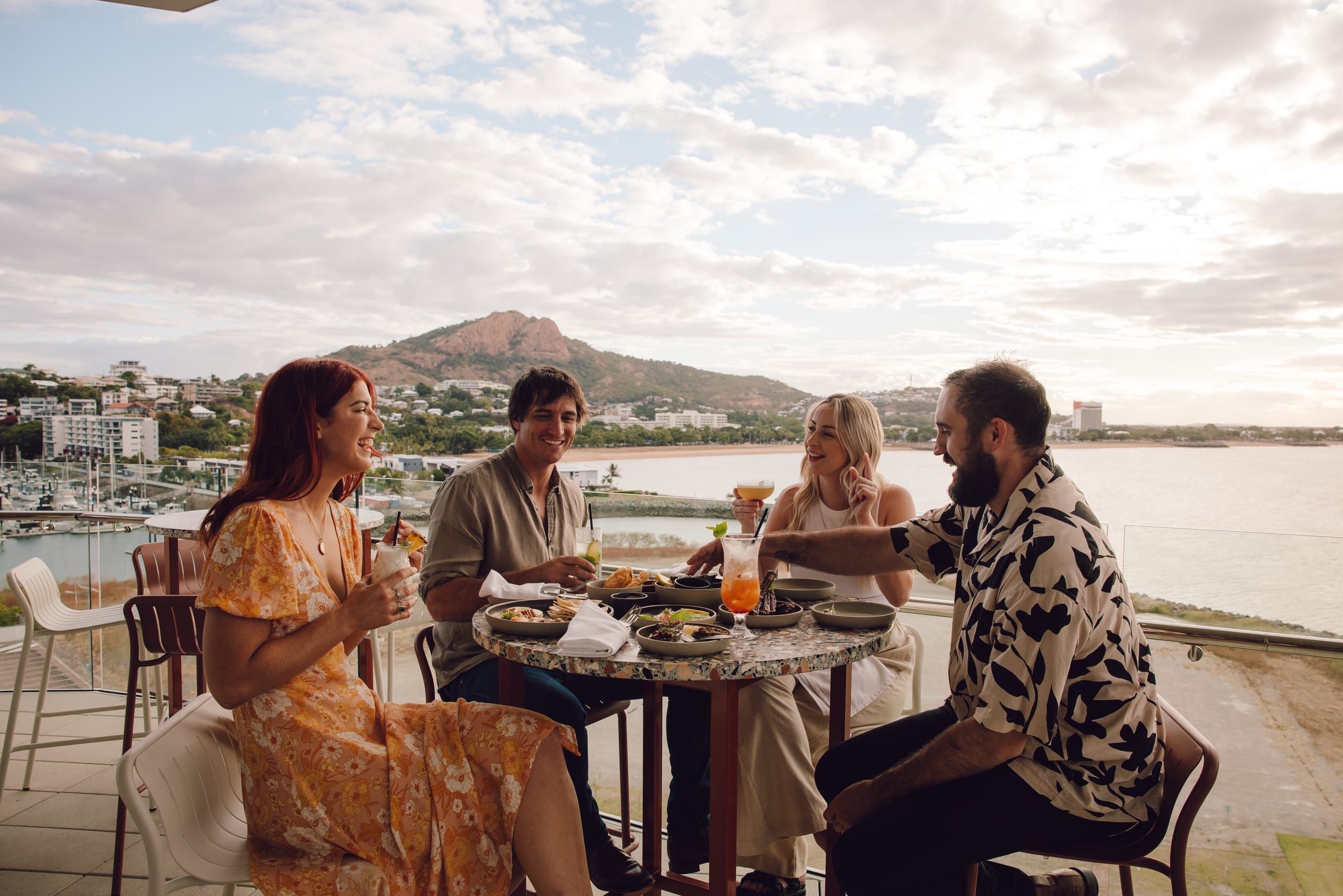 four friends enjoying cocktails and food at a rooftop bar overlooking Townsville's waterfront and Castle Hill