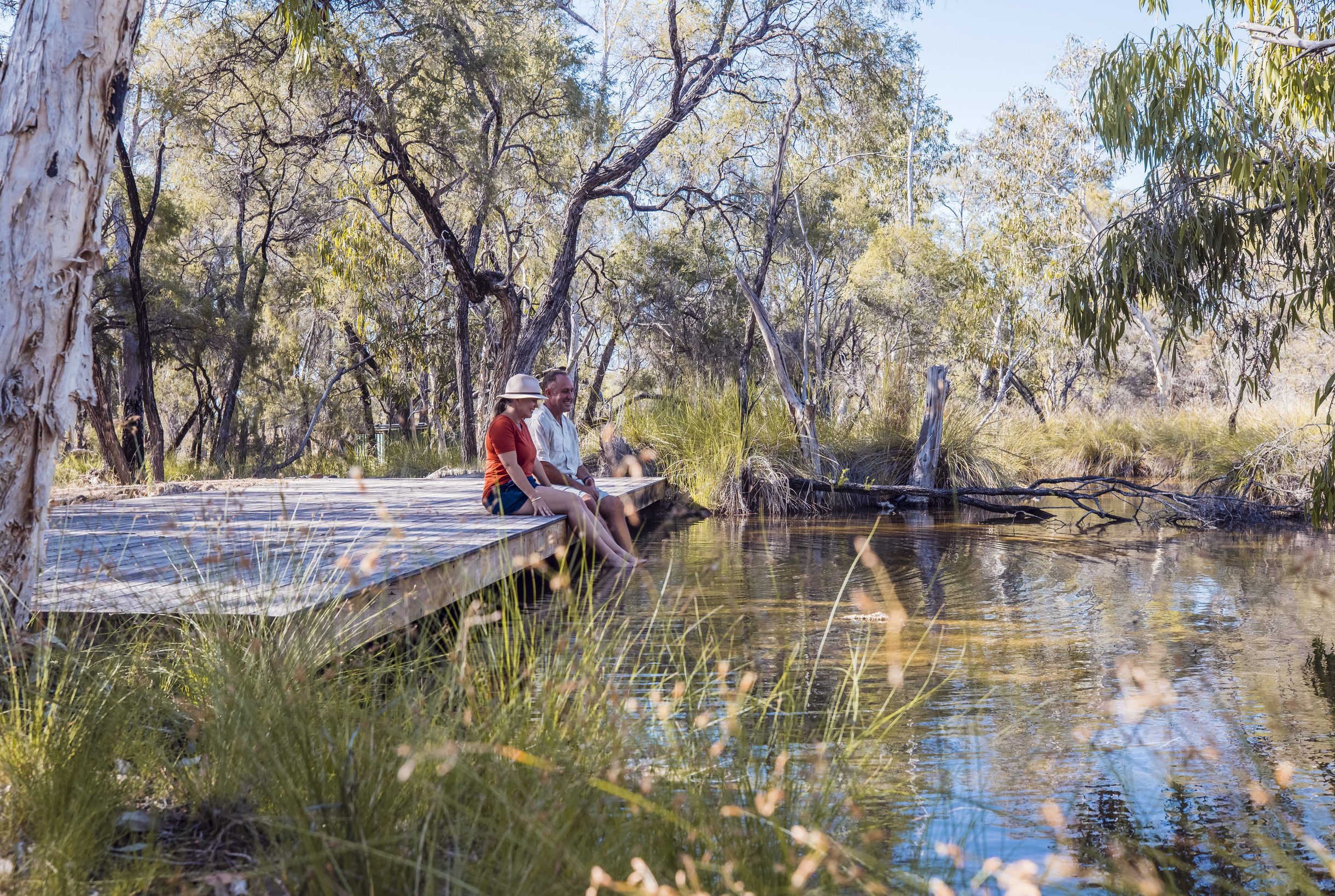 Couple sitting at the edge of Talaroo Hot Springs with toes dipping in the water