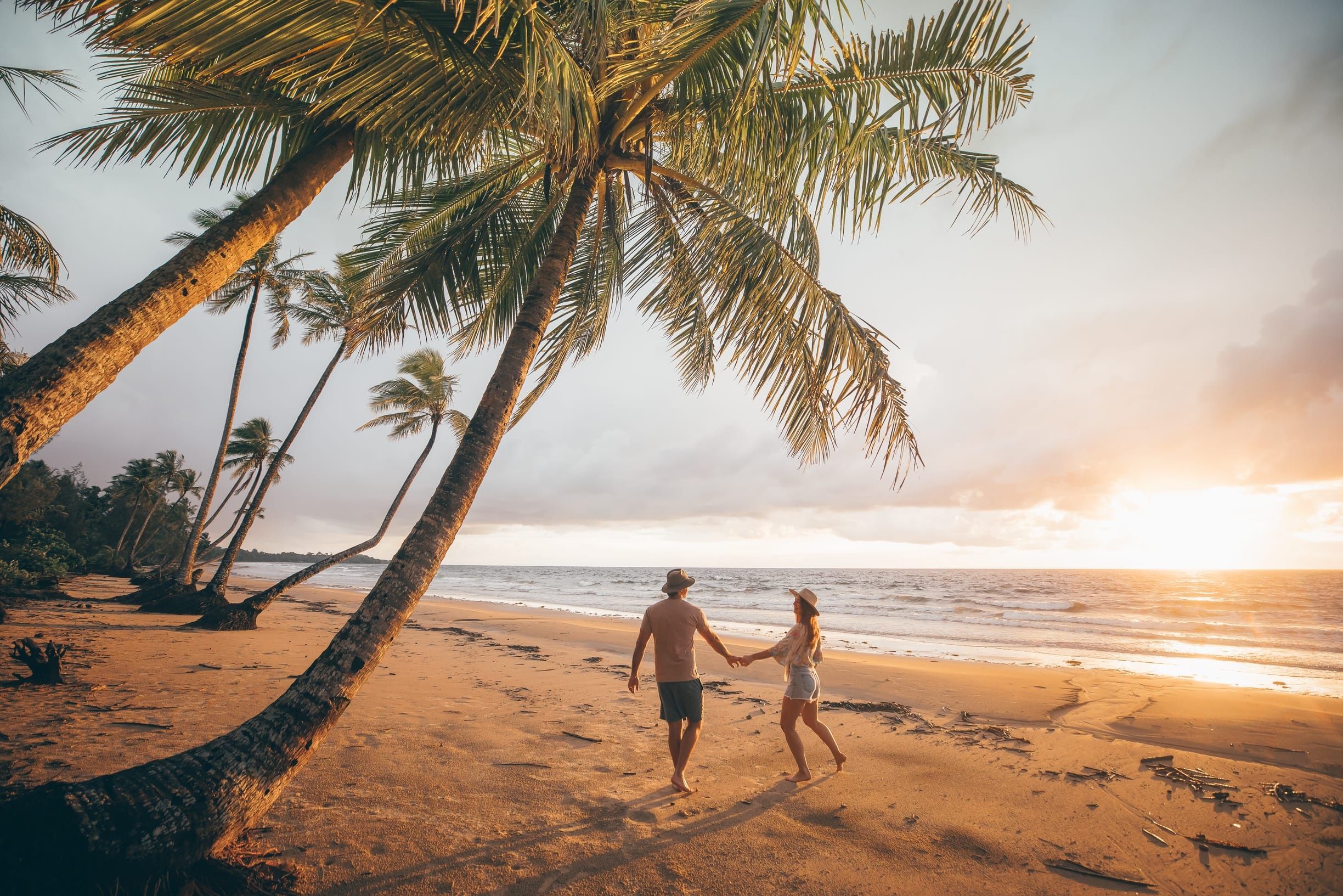 Couple hold hands walking on the beach at sunset