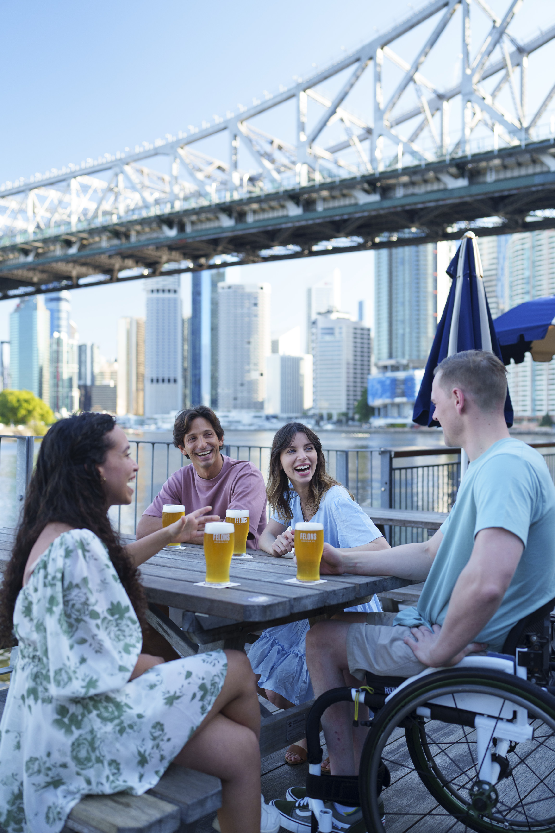 Group of friends enjoy waterfront beers at Felons Brewing Co, with city skyline and Story Bridge in background