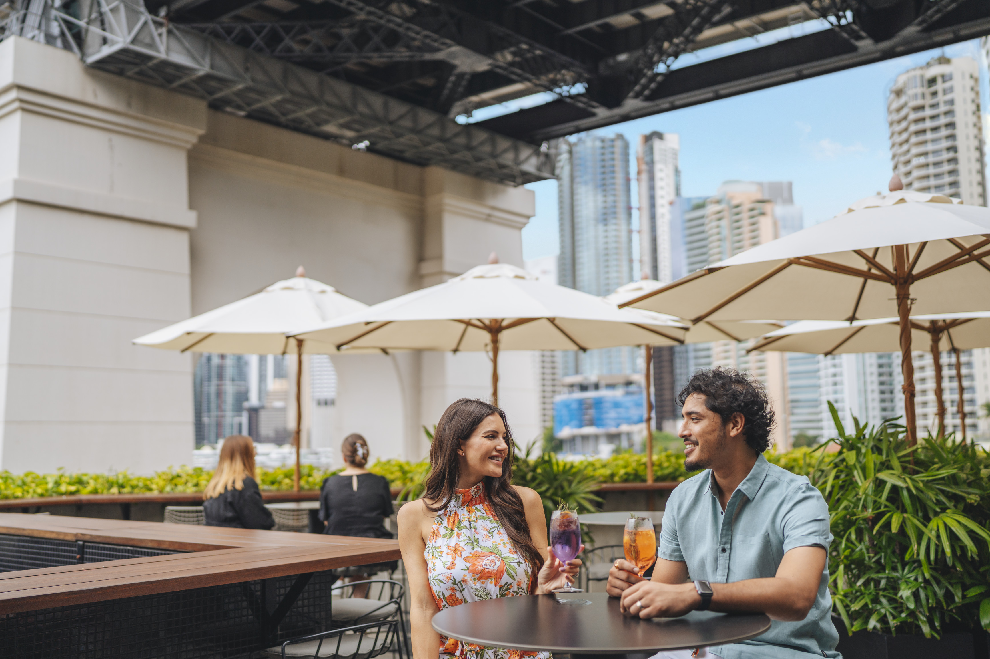 Couple enjoying a drink at Fiume Rooftop Bar at Crystalbrook Vincent, with the Story Bridge and Brisbane City in the background