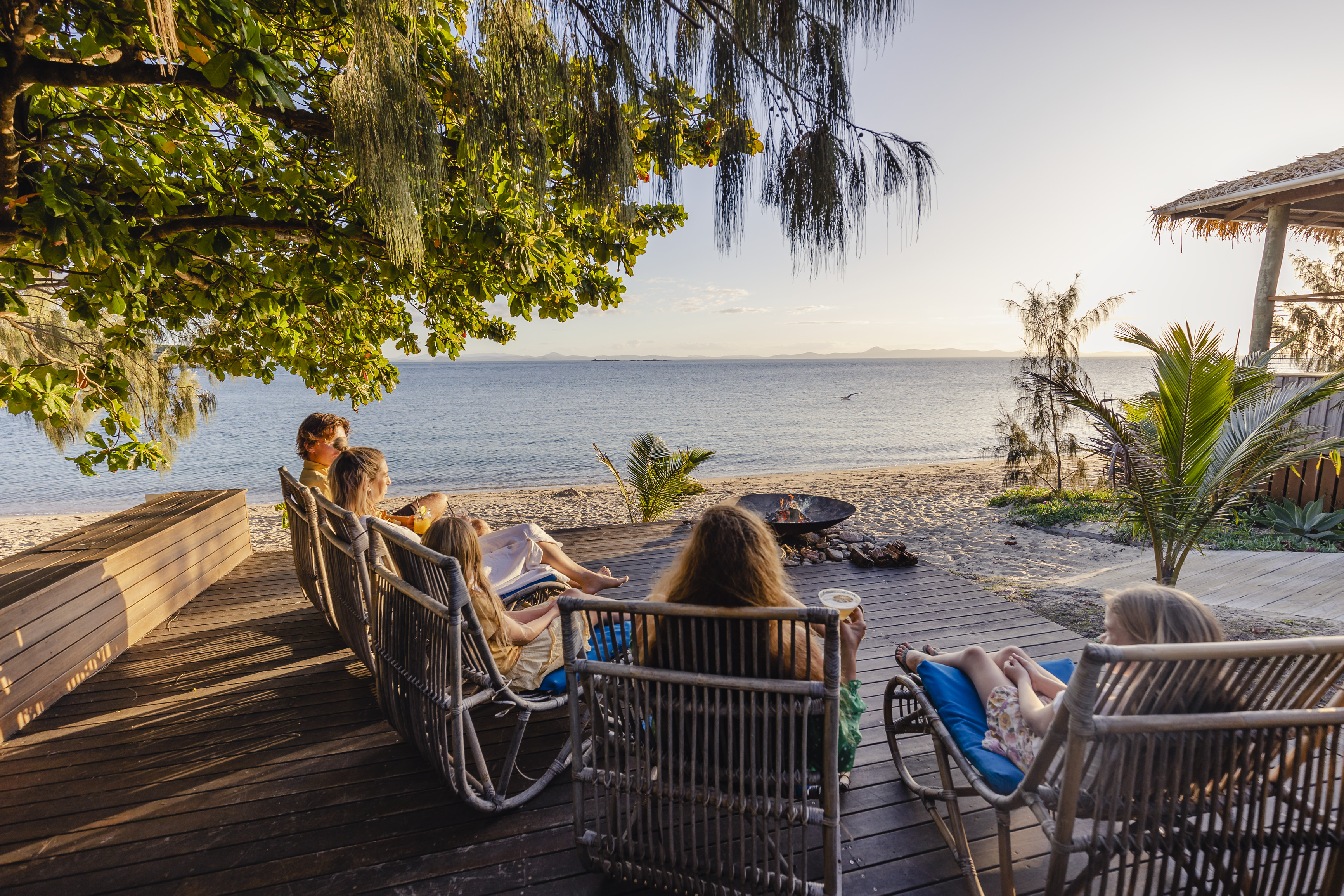 Family enjoying drinks around the beachfront bonfire at sunset, Pumpkin Island, Southern Great Barrier Reef