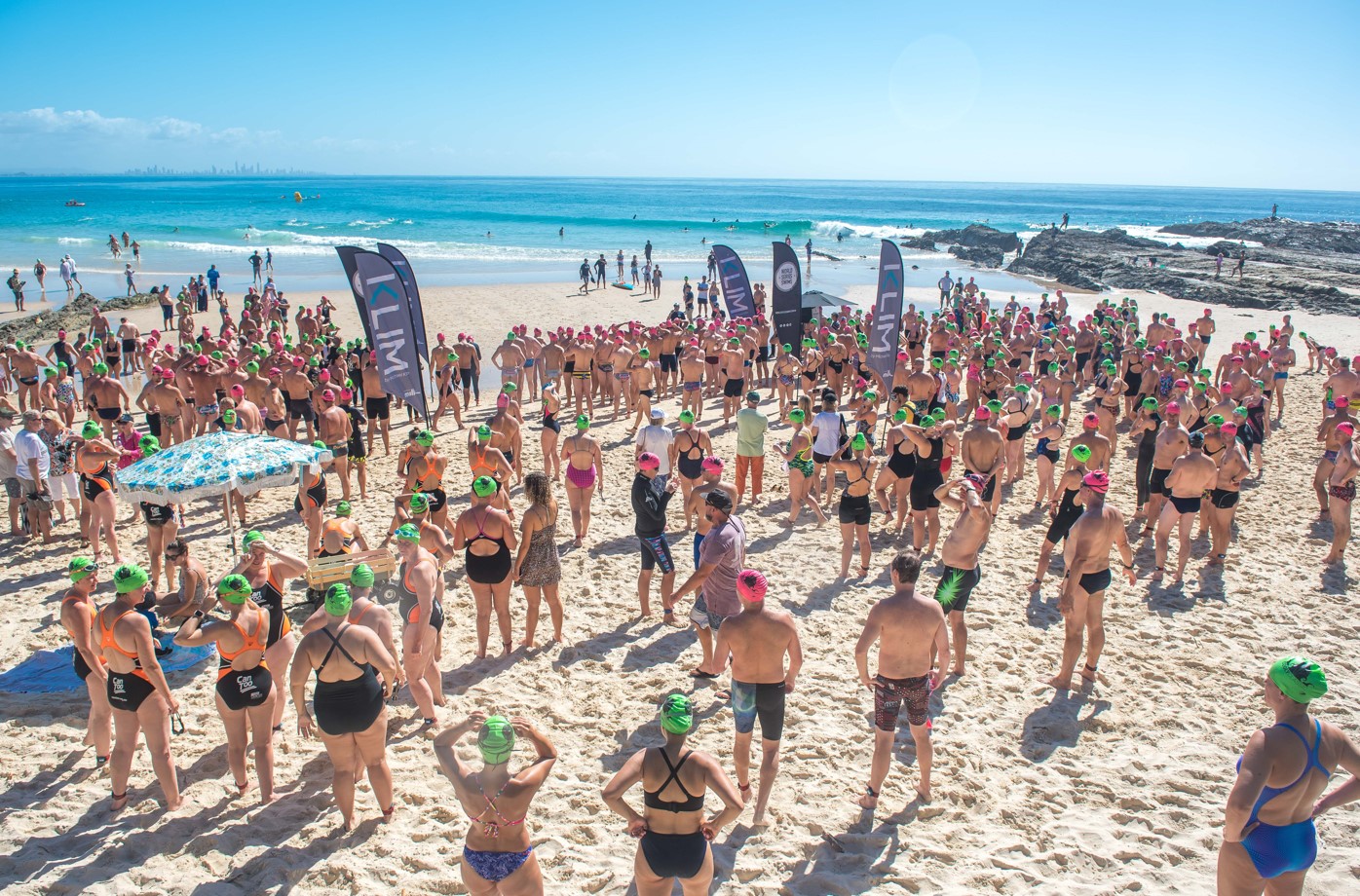 A huge group of swimmers wearing green and pink swimming caps have gathered at the oceans edge at the Cooly Classic Event on the Gold Coast.