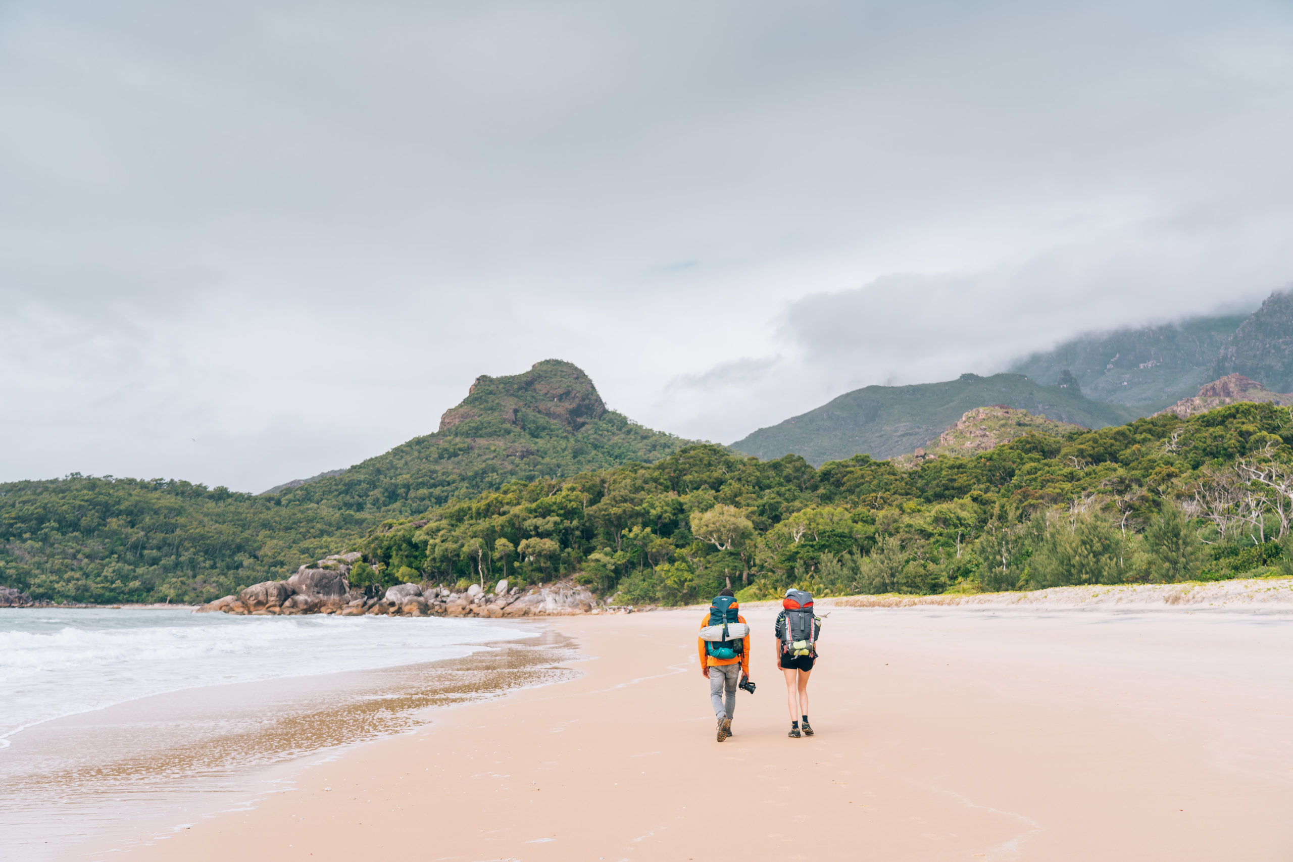 Two people hiking with backpacks on a beach