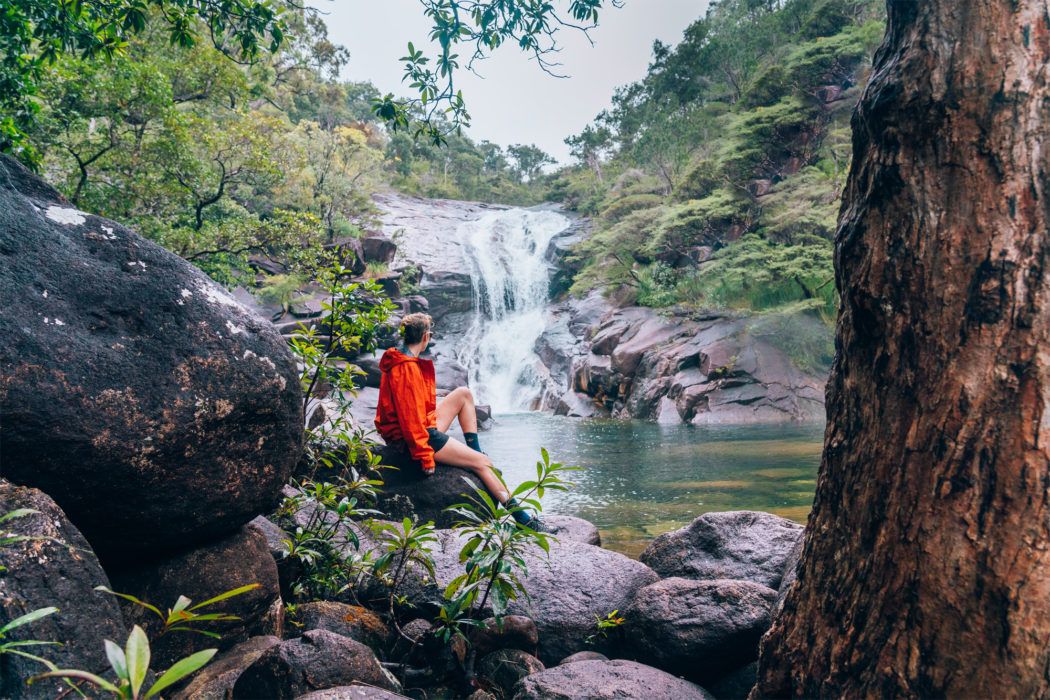 A solo hiker sits looking at the view of a waterfall A solo hiker sits looking at the view of a waterfall